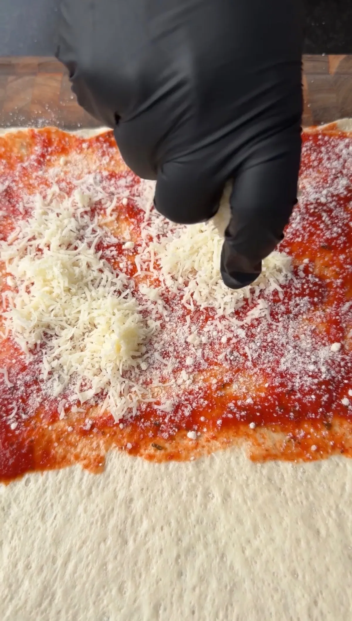 Gloved hand sprinkling freshly grated mozzarella and Parmesan over marinara sauce on rolled Pillsbury pizza dough