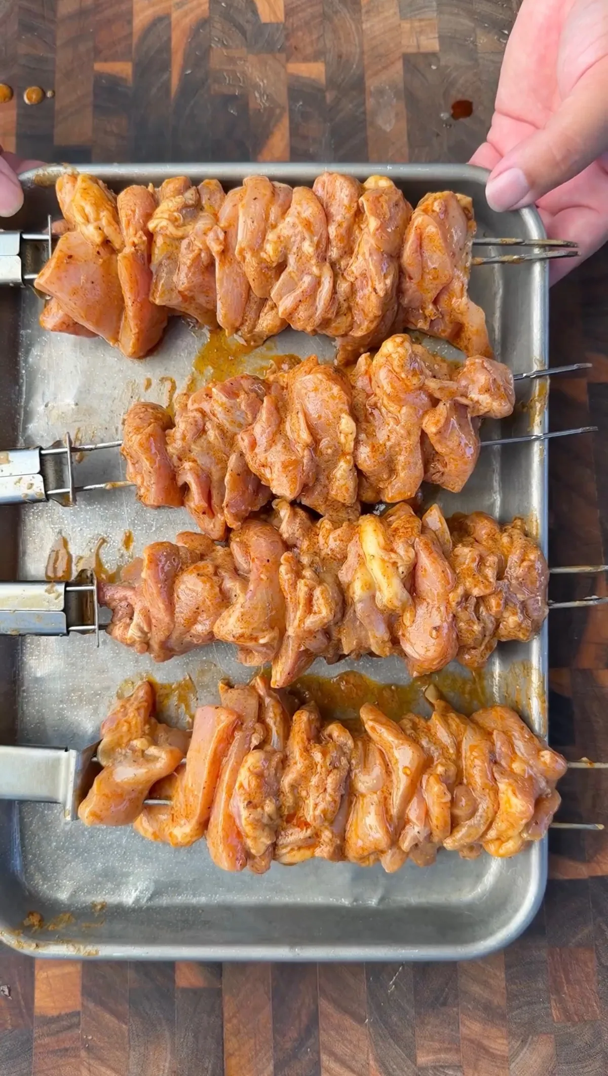 Raw marinated chicken thighs threaded on metal skewers on a sheet pan, coated in chili-lime marinade