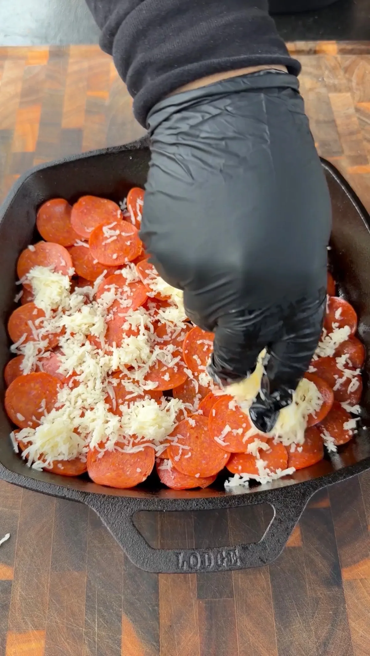 Shredded mozzarella cheese being added over pepperoni layer in a Lodge cast-iron skillet for upside-down deep dish pizza