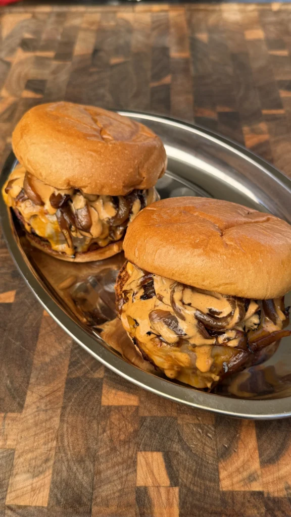 Two juicy cheeseburgers loaded with sautéed mushrooms and melted cheese sauce on brioche buns, served on a silver tray