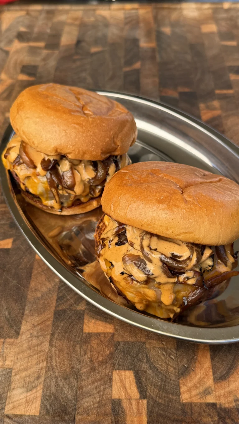 Two juicy cheeseburgers loaded with sautéed mushrooms and melted cheese sauce on brioche buns, served on a silver tray