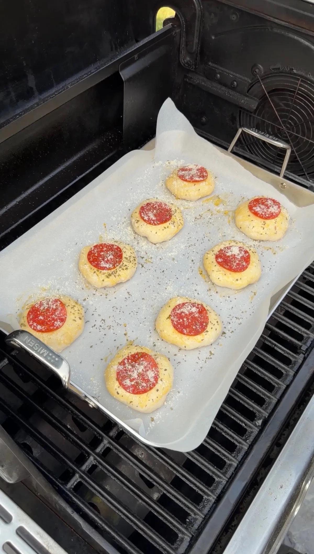 Eight unbaked pepperoni pizza bombs on parchment paper, sprinkled with herbs and Parmesan, on a grill pan