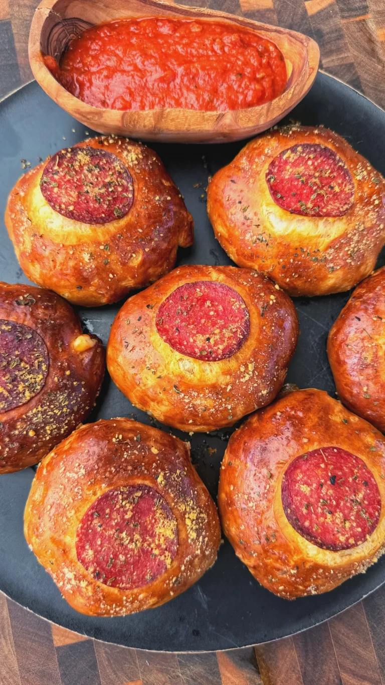 Golden baked pepperoni pizza bombs topped with Italian seasoning on a dark plate with marinara dipping sauce