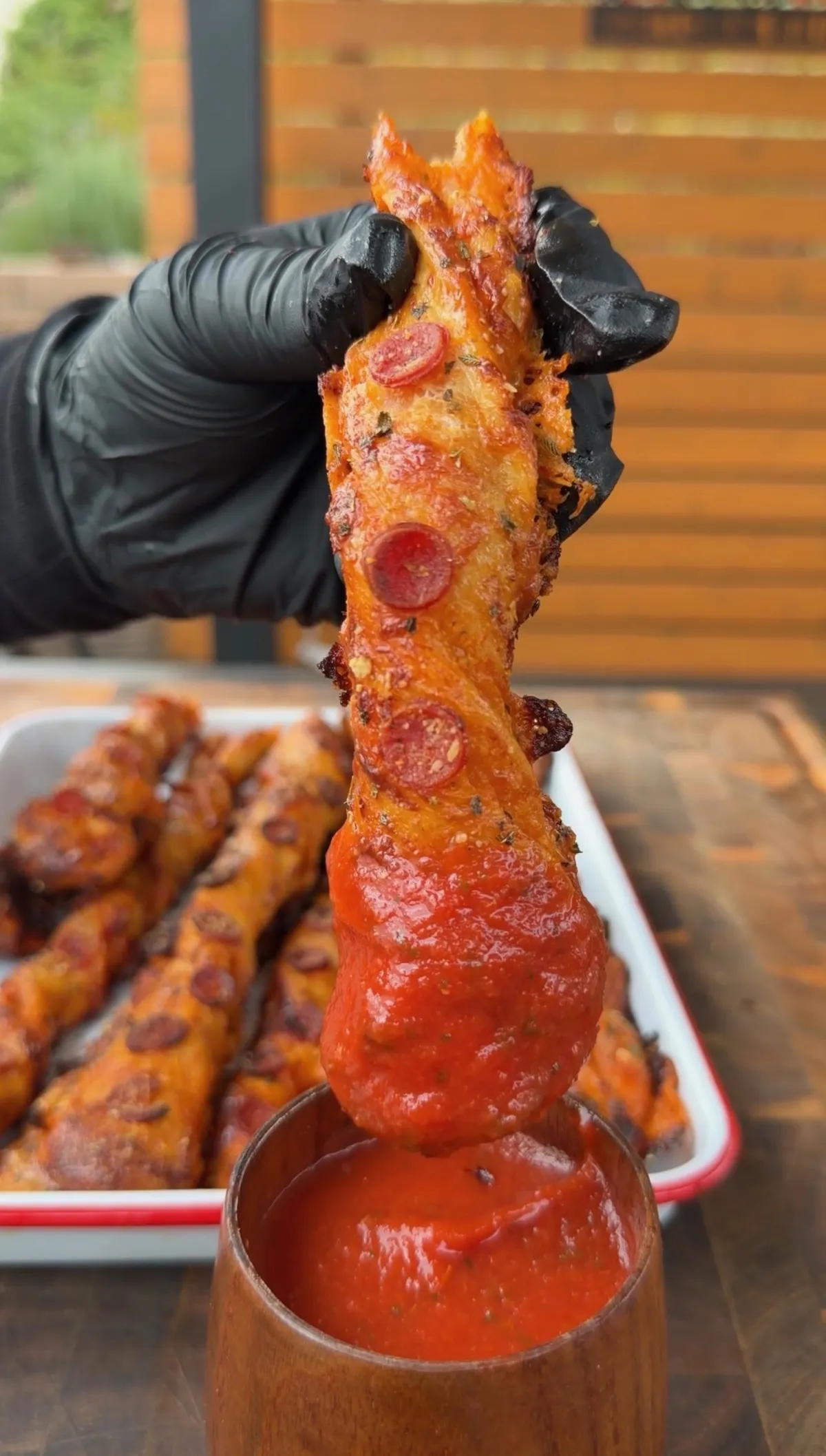 Hand dipping a golden twisted pepperoni pizza twist with mini pepperonis and oregano into a cup of marinara sauce