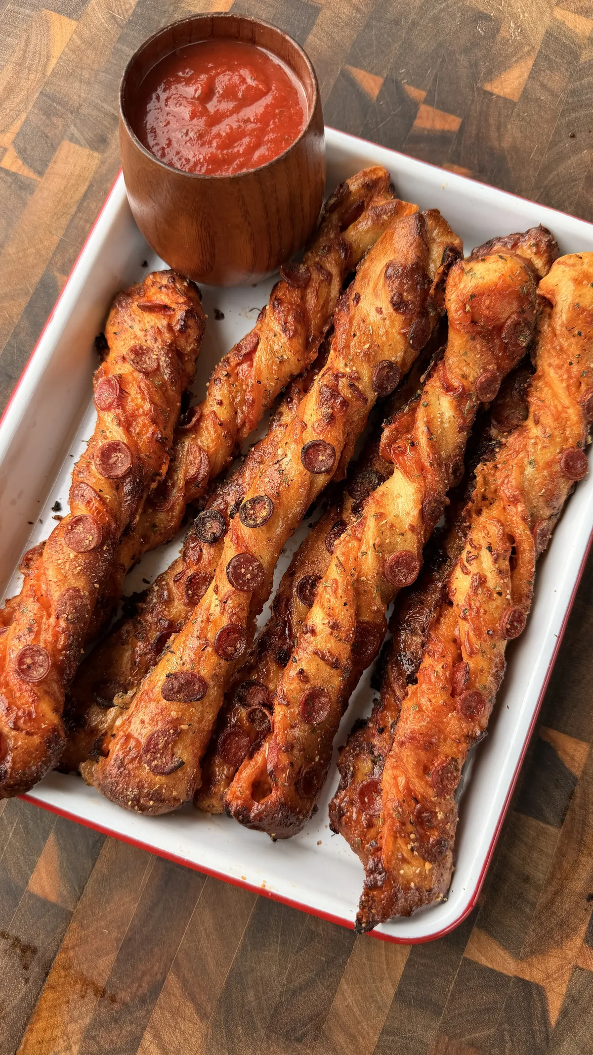 Golden-baked pepperoni pizza twists with mini pepperonis and oregano on a white tray with marinara dipping sauce