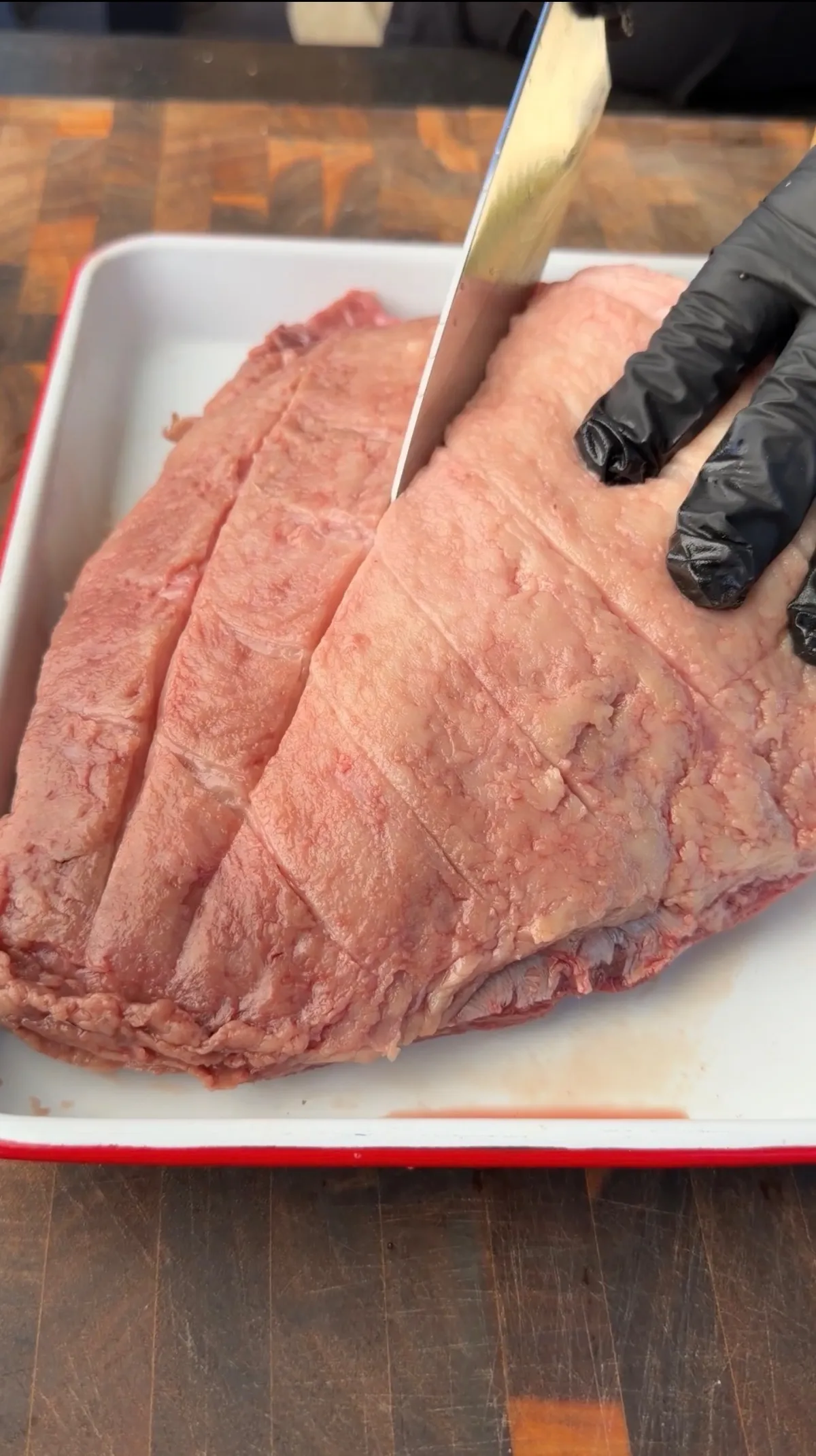 Raw picanha sirloin cap with crosshatch-scored fat cap being prepared in a white baking dish with a knife