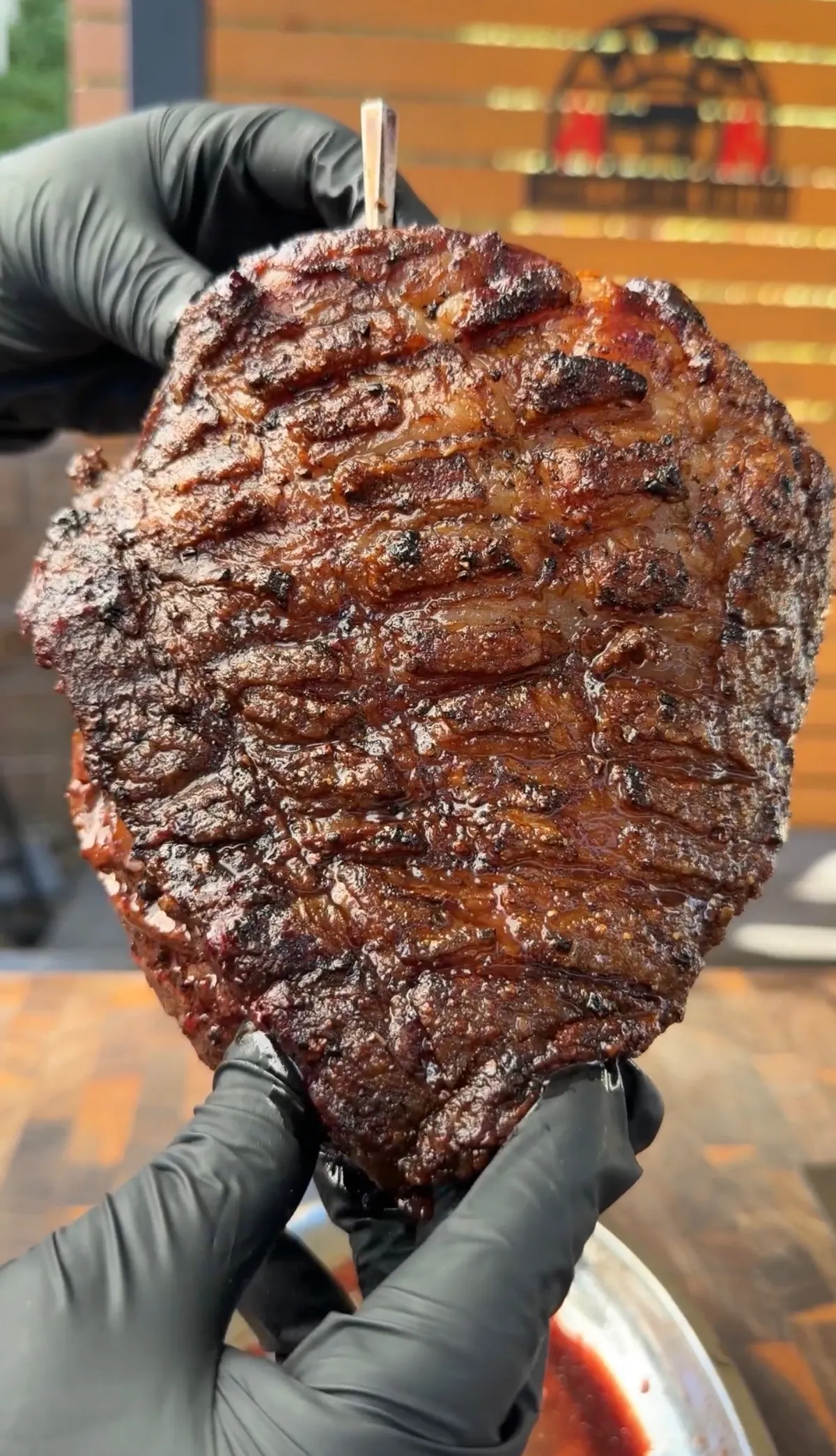 Whole seared picanha with scored crosshatch fat cap held in black gloves, showing golden-brown crust after cast-iron searing