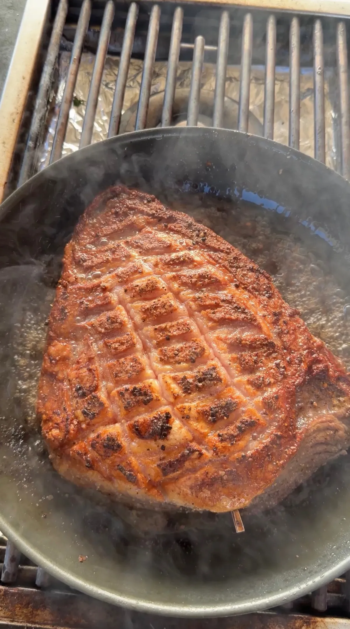 Scored picanha fat cap searing fat-side down in a cast-iron skillet on a grill, developing a golden-brown crust
