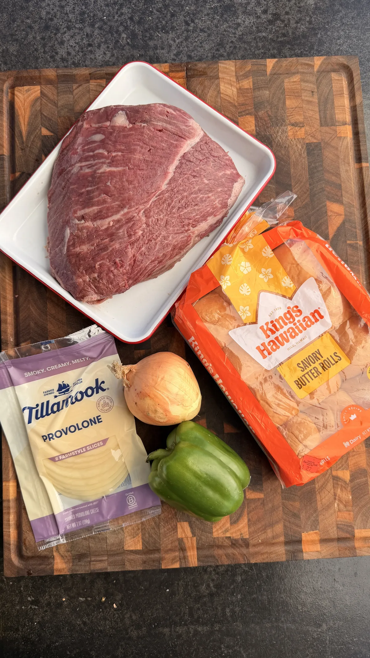 Picanha, King's Hawaiian savory butter rolls, Tillamook provolone, sweet onion, and green bell pepper on a wood cutting board