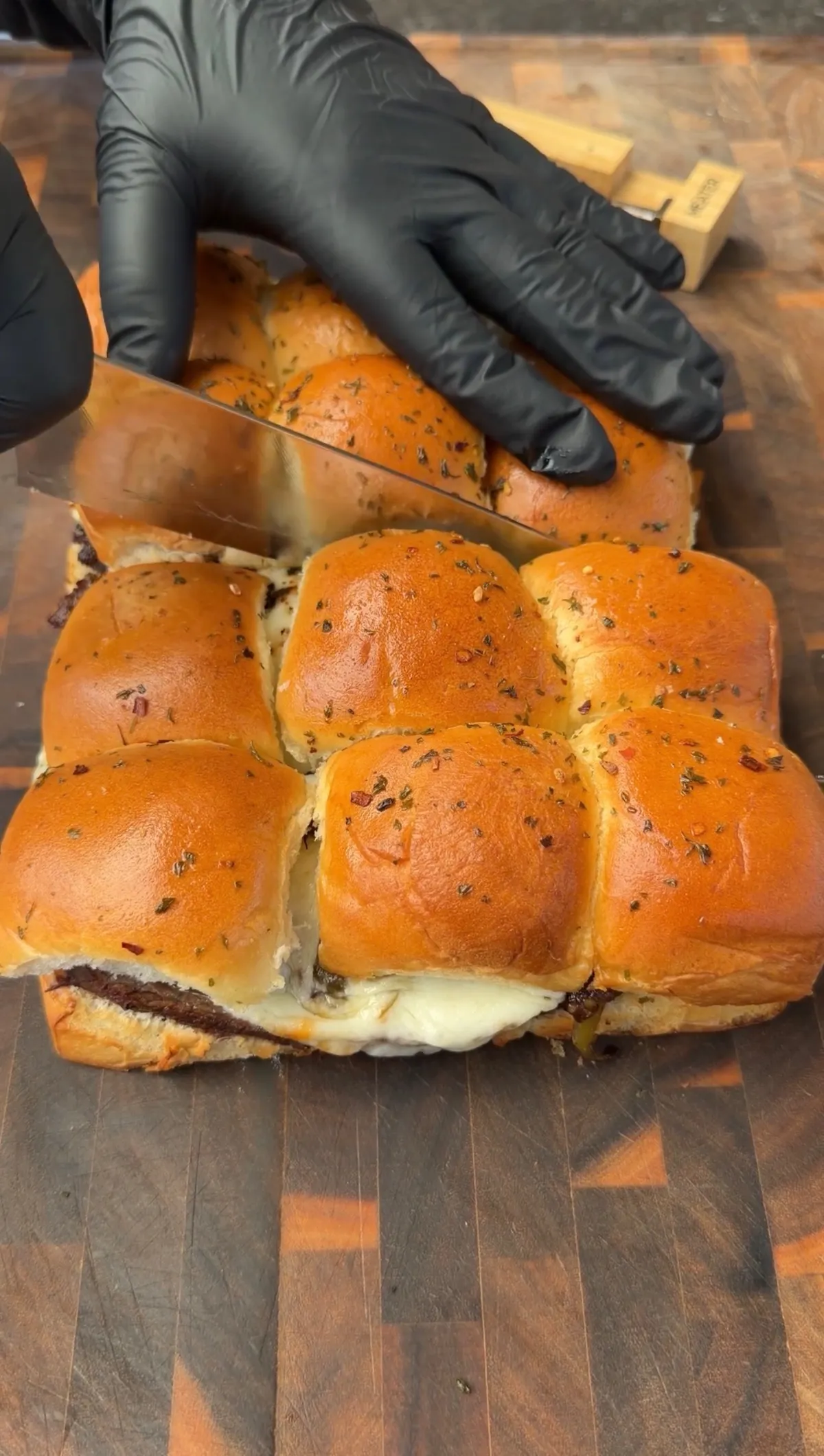 Toasted King's Hawaiian roll sliders with melted provolone and picanha being sliced on a wood cutting board