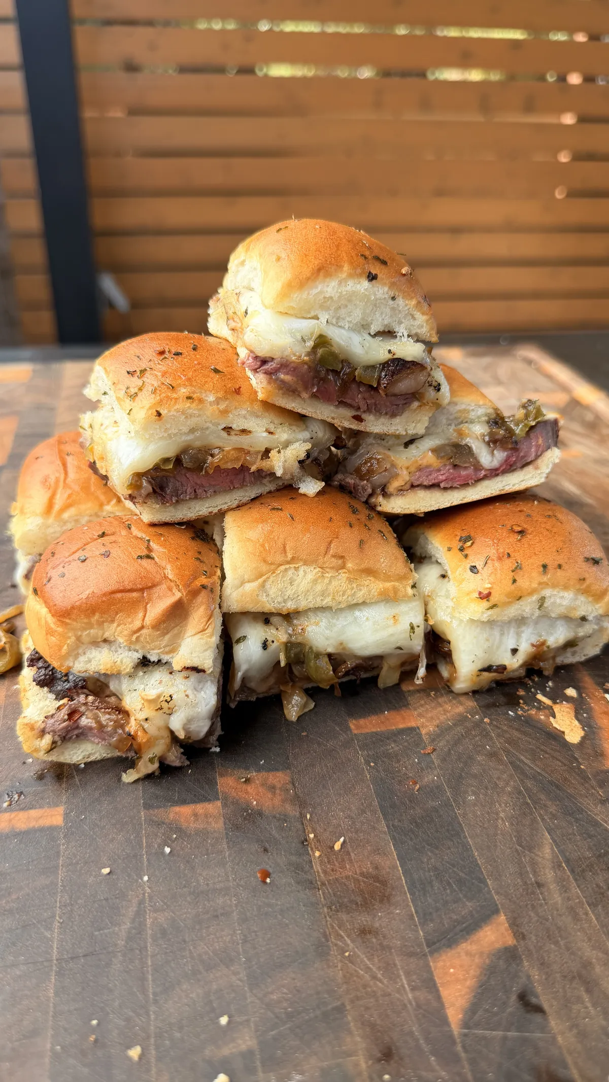 Stacked picanha steak sliders on toasted King's Hawaiian rolls with melted provolone, sautéed peppers and onions on a wood cutting board