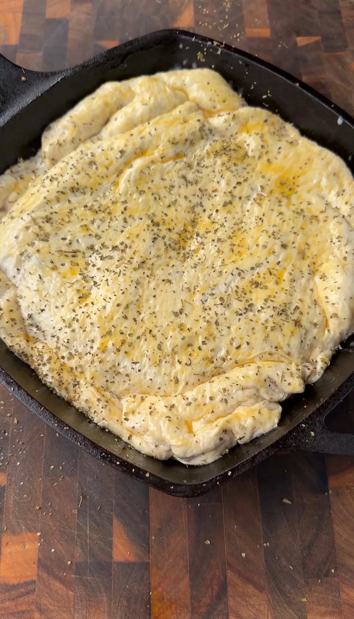 Pillsbury pizza dough brushed with egg wash and sprinkled with oregano in a square cast-iron skillet, ready to bake