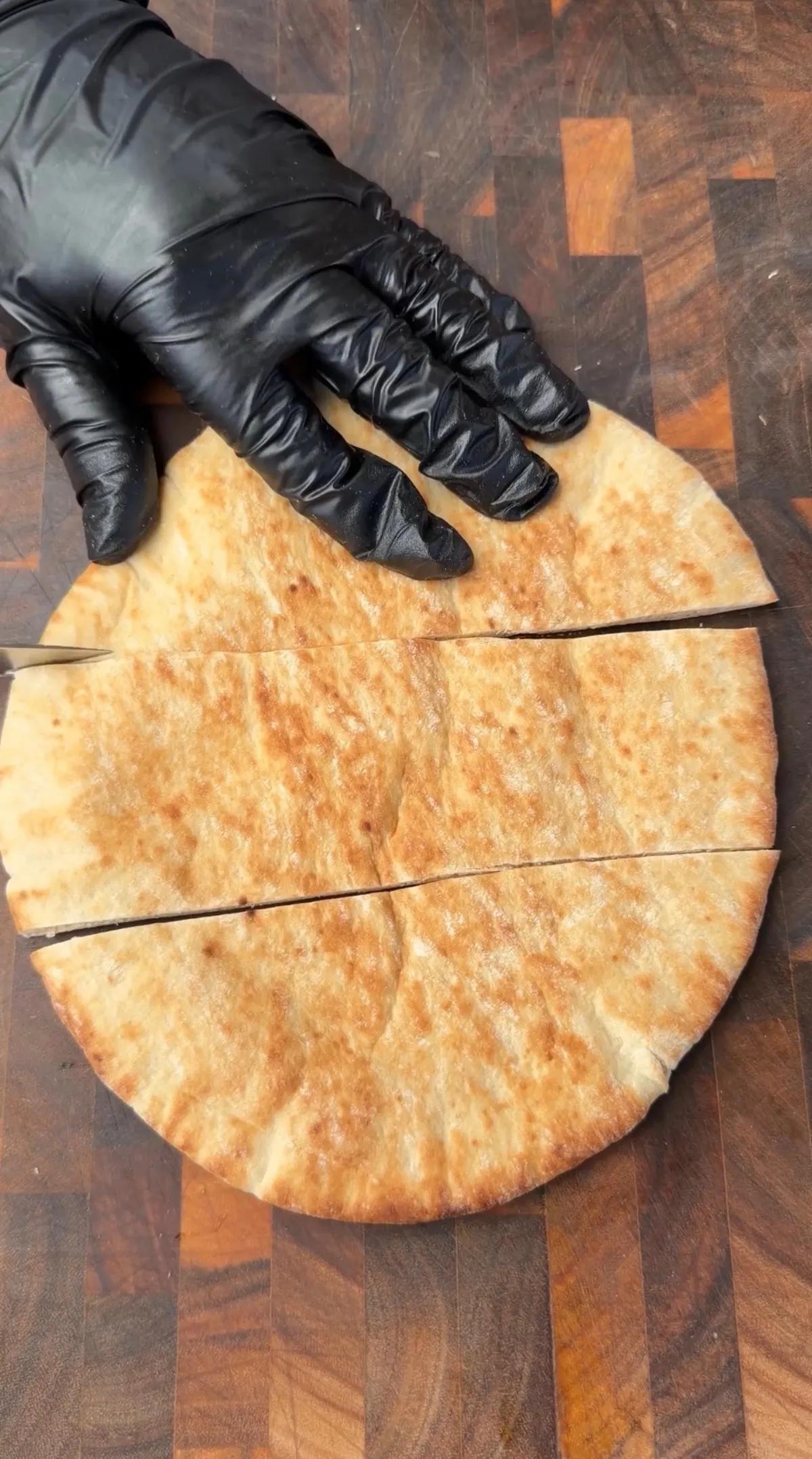 Thick pita bread cut in half to create pockets for arayes, held on a wooden board with a black-gloved hand
