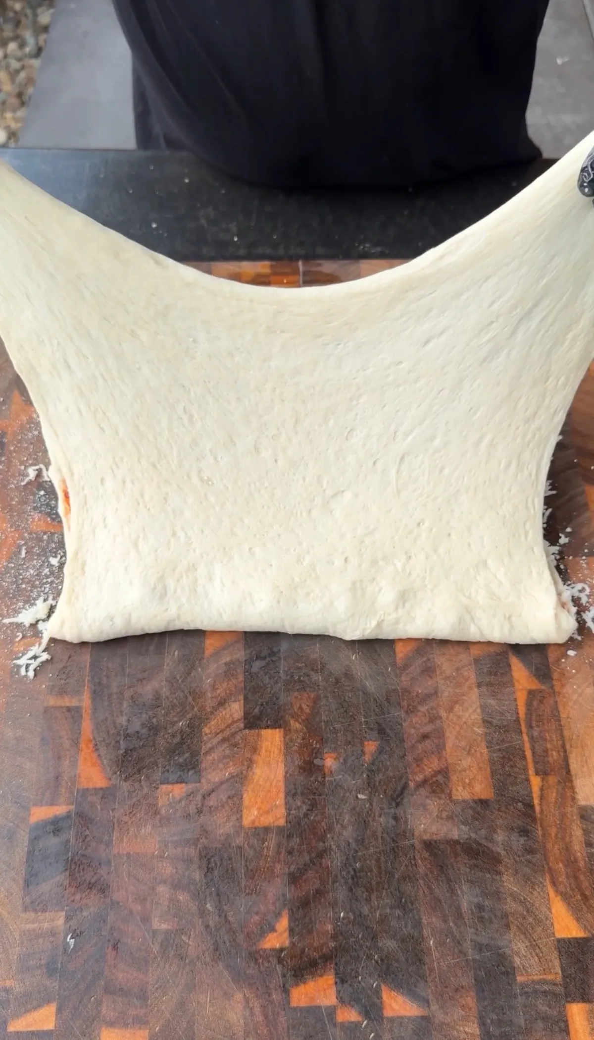 Pillsbury pizza dough being stretched into a large rectangle on a wood cutting board for pepperoni pizza twists