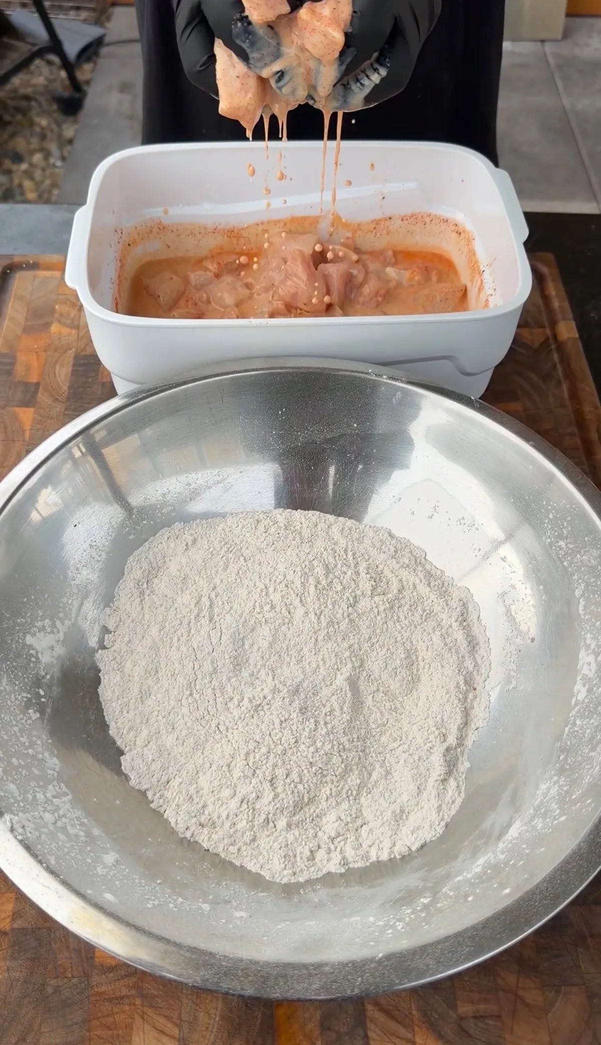 Marinated chicken pieces being transferred from spiced buttermilk bath to bowl of seasoned flour for popcorn chicken
