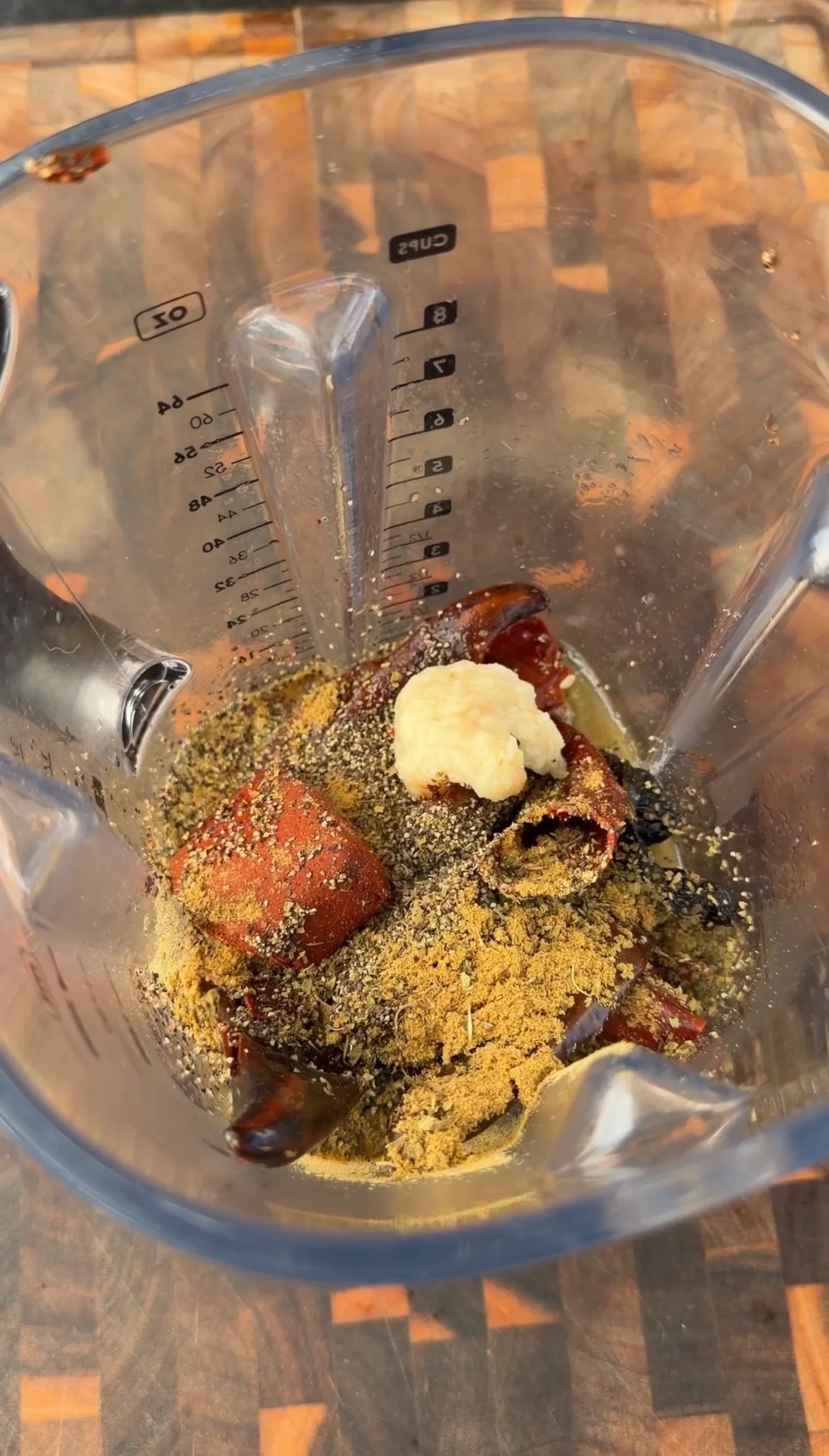 Blender jar with dried chilies, ground cumin, herbs, and minced garlic for pork belly porchetta seasoning blend