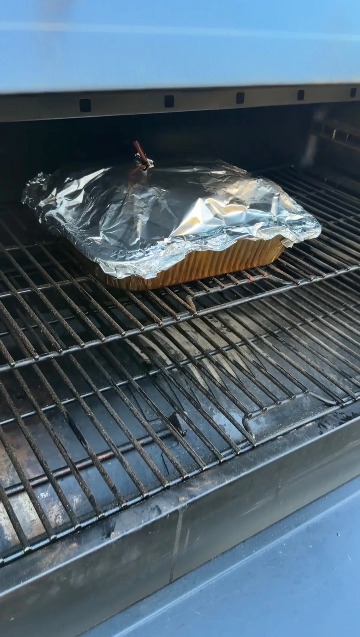 Bone-in pork shoulder wrapped tightly in foil in a tray on a smoker grill at 350°F until probe-tender