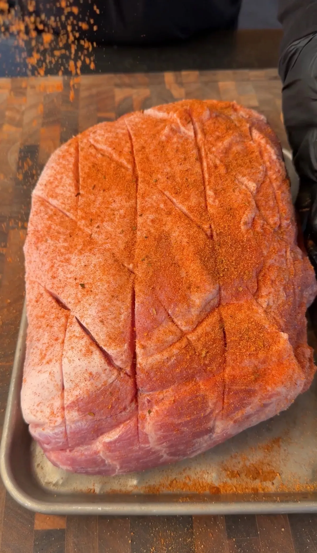 Bone-in pork shoulder with crosshatch-scored fat cap generously seasoned with sweet BBQ rub on a sheet pan