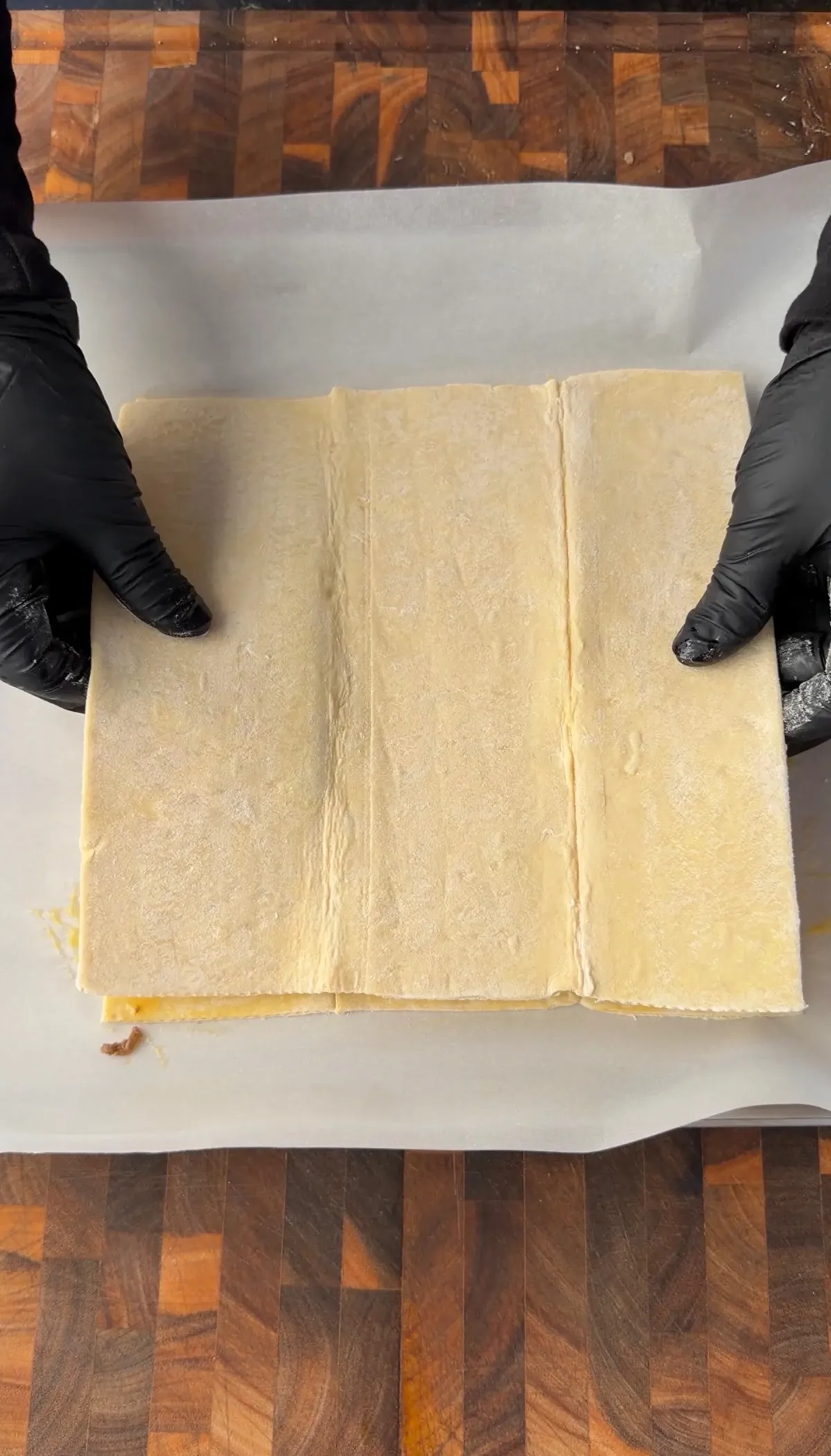 Hands in black gloves folding puff pastry dough over cheeseburger hot pocket filling on parchment paper