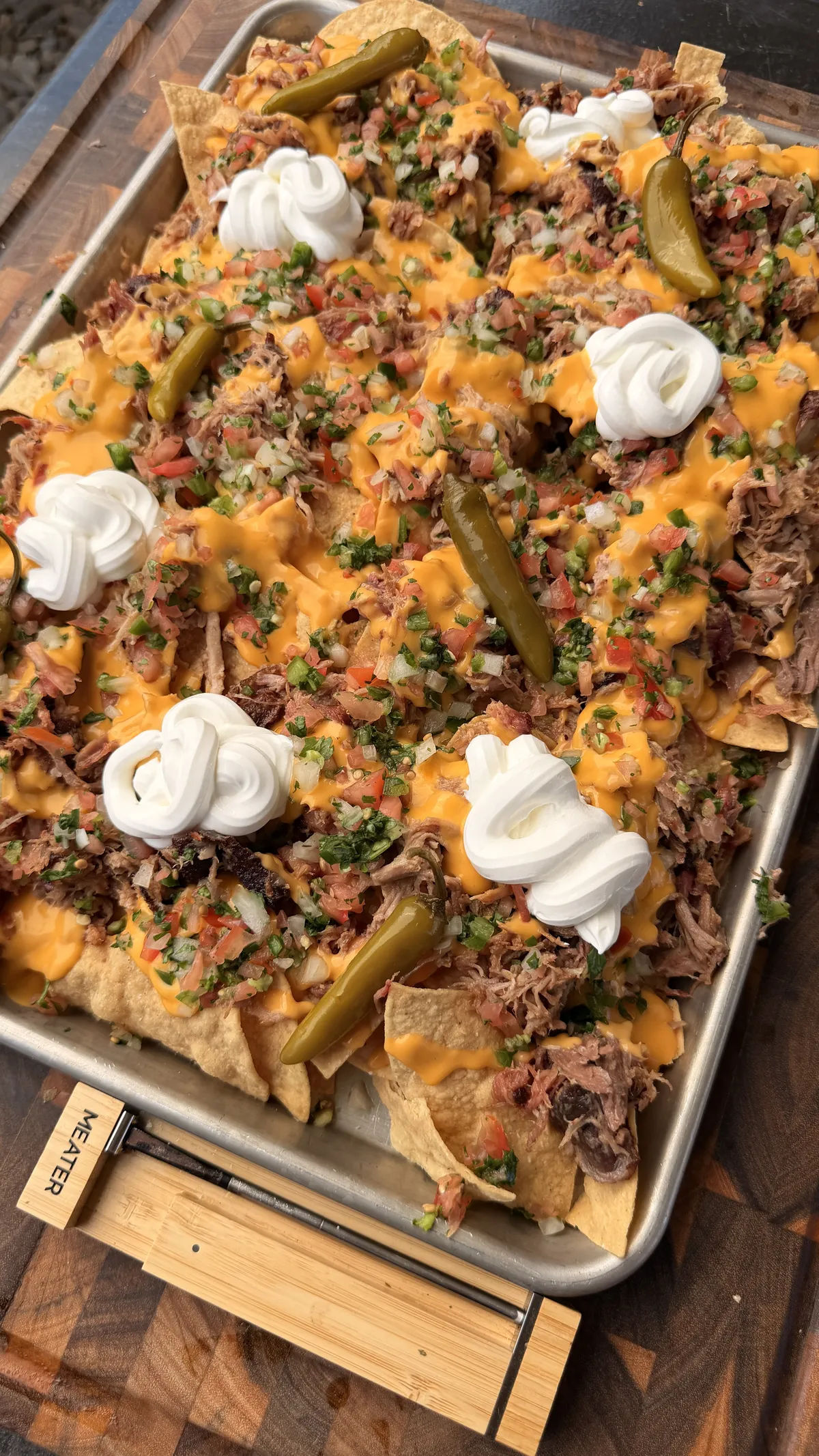 Sheet pan pulled pork nachos with nacho cheese sauce, pico de gallo, sour cream, and pickled jalapeños