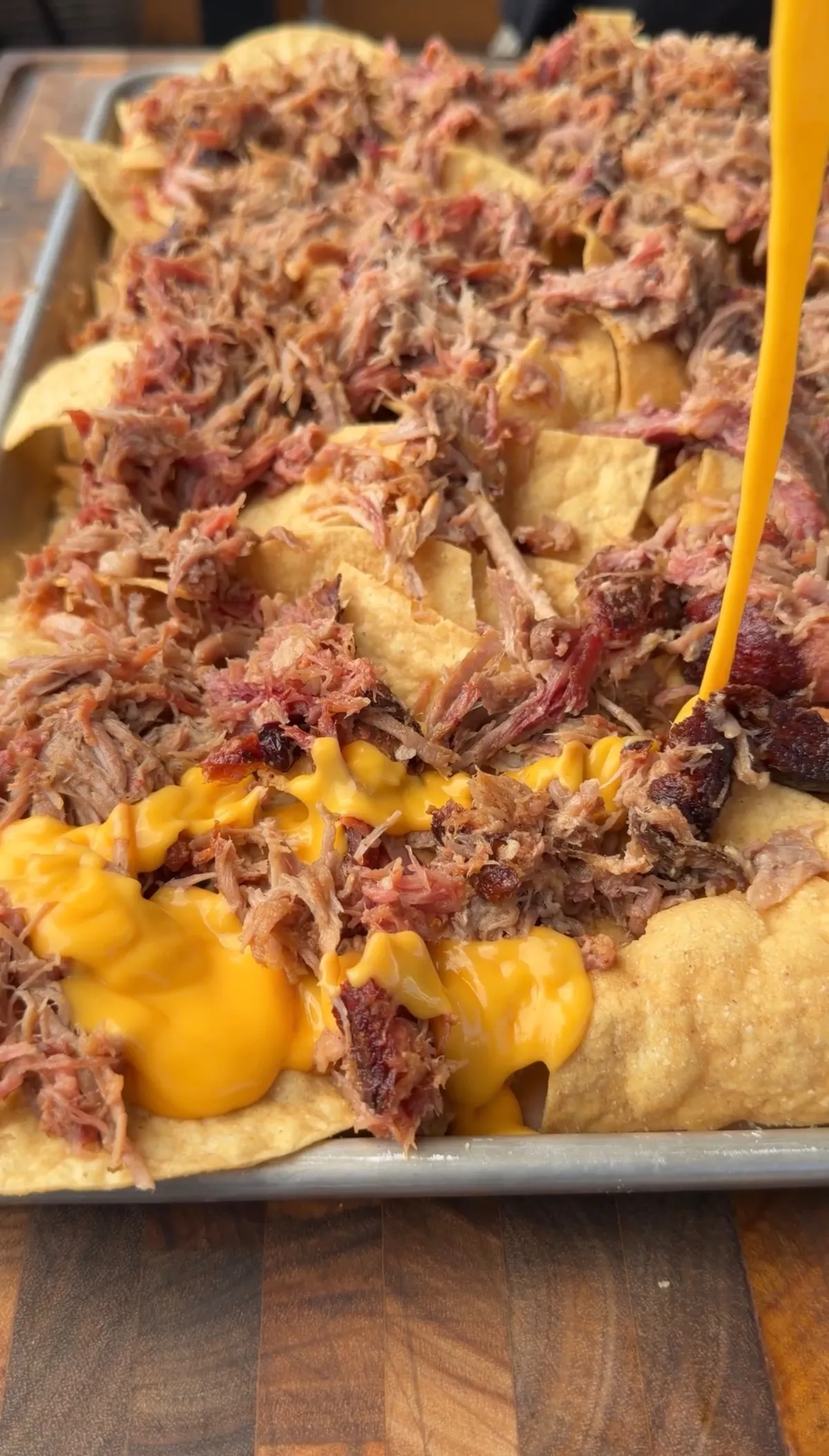 Tailgating pulled pork nachos on a baking sheet loaded with smoked pulled pork and warm nacho cheese sauce