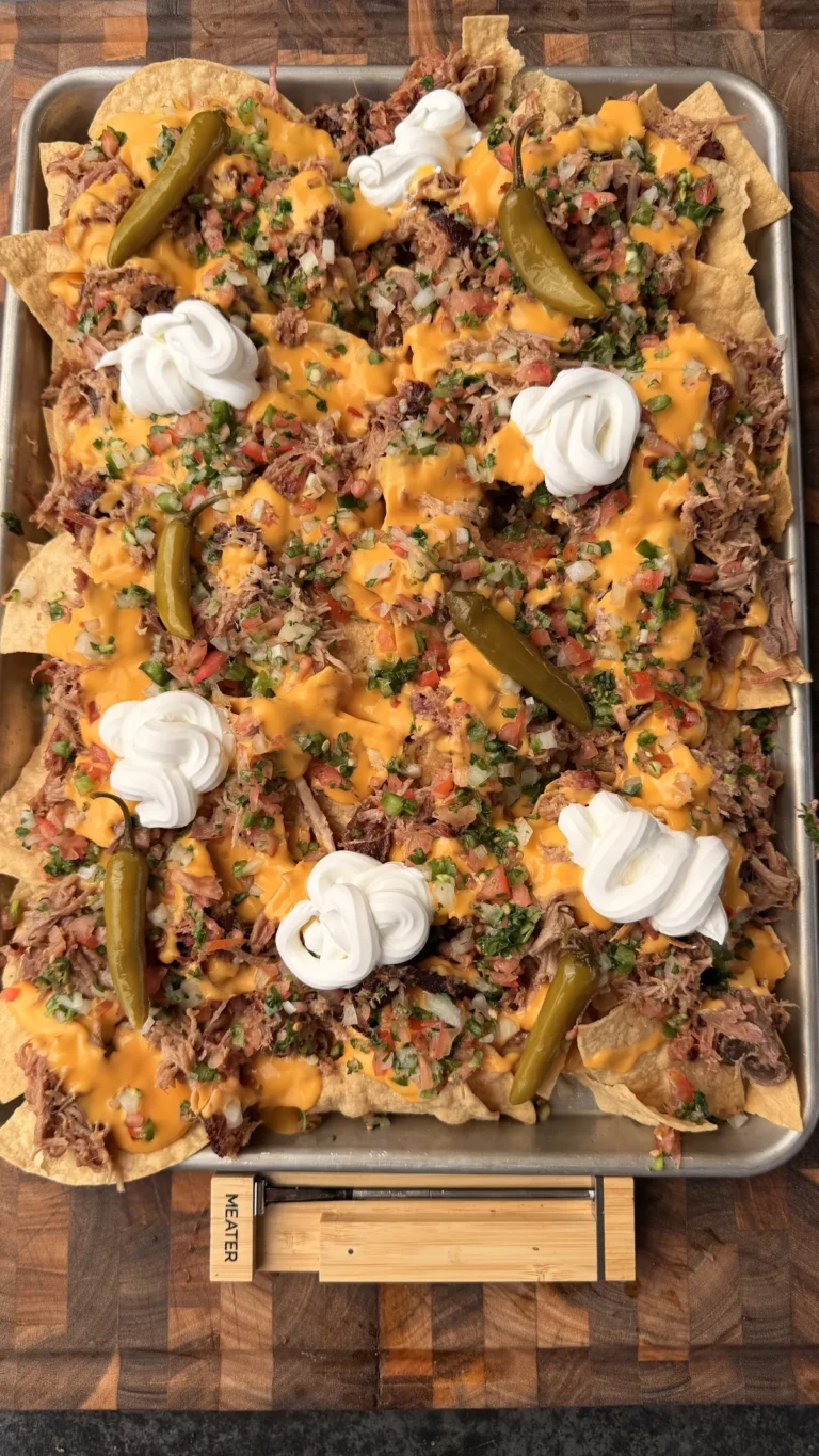 Sheet pan pulled pork nachos loaded with nacho cheese sauce, pico de gallo, sour cream, and pickled jalapeños