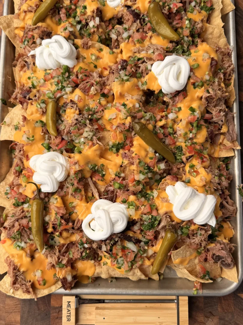 Sheet pan pulled pork nachos loaded with nacho cheese sauce, pico de gallo, sour cream, and pickled jalapeños