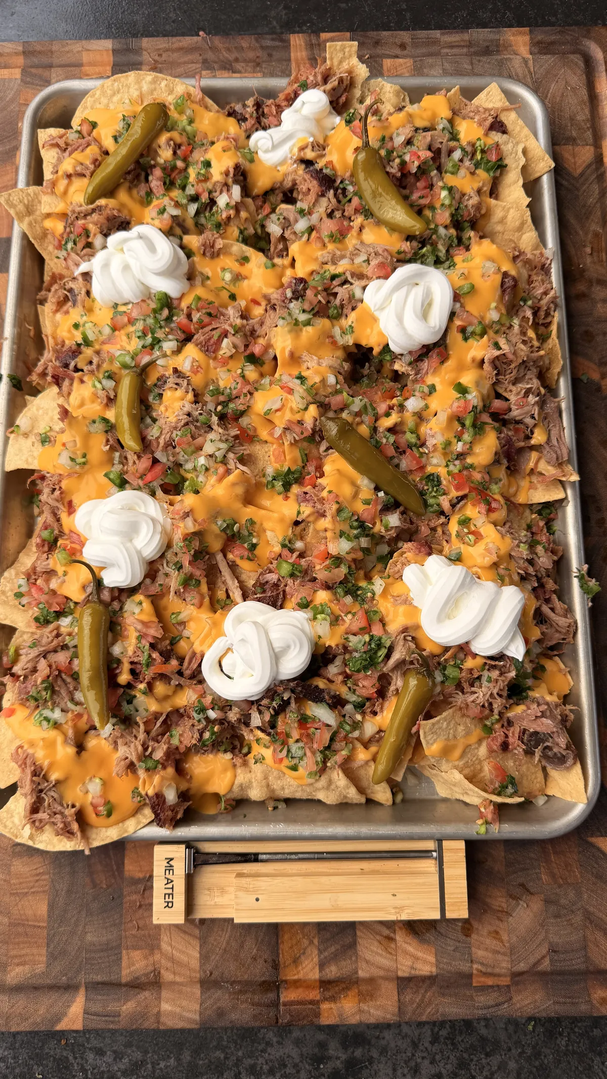 Sheet pan pulled pork nachos topped with nacho cheese sauce, pico de gallo, sour cream, and pickled jalapeños