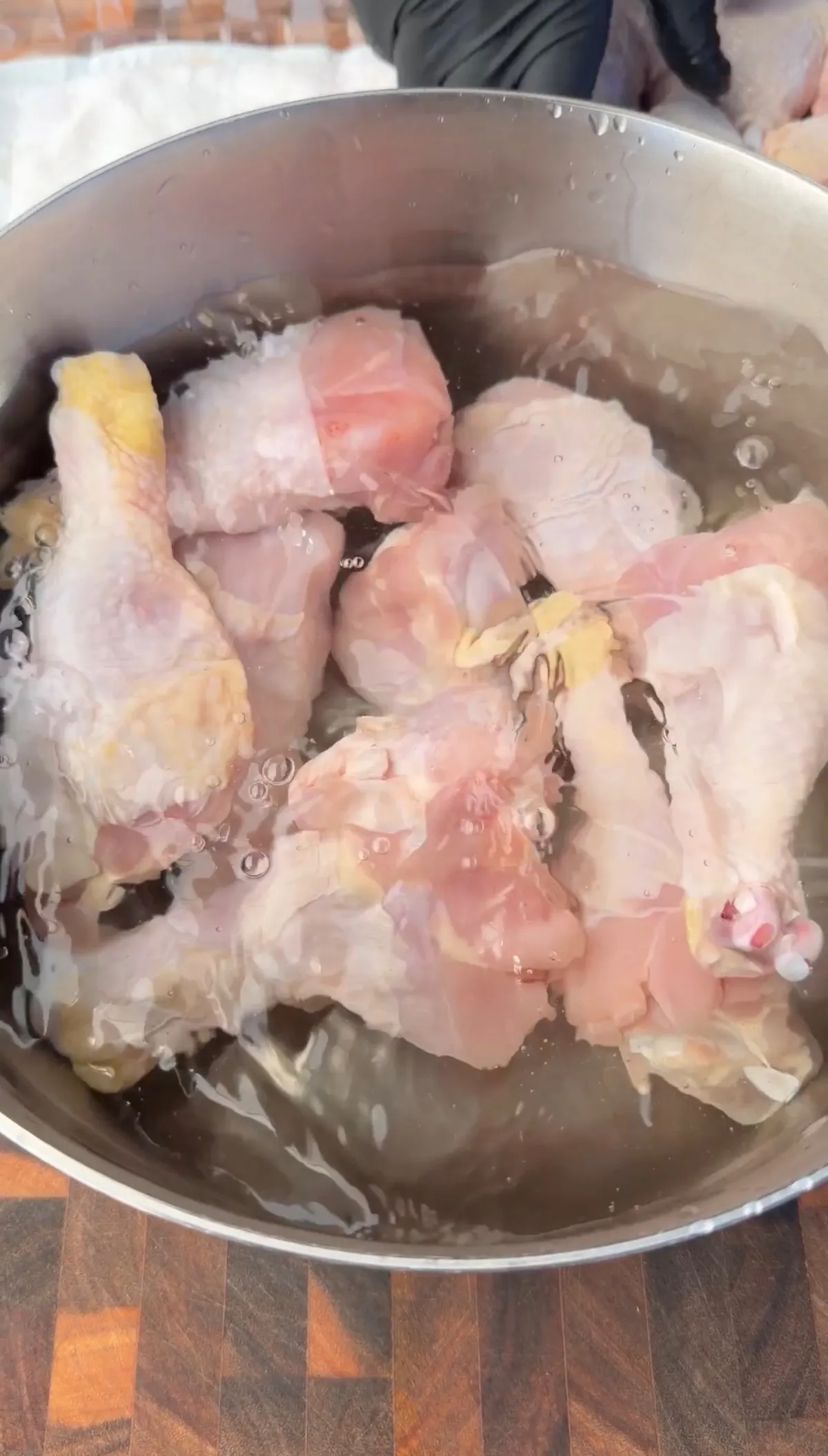 Raw chicken drumsticks submerged in water in a large stainless steel pot, ready to boil for 45 minutes