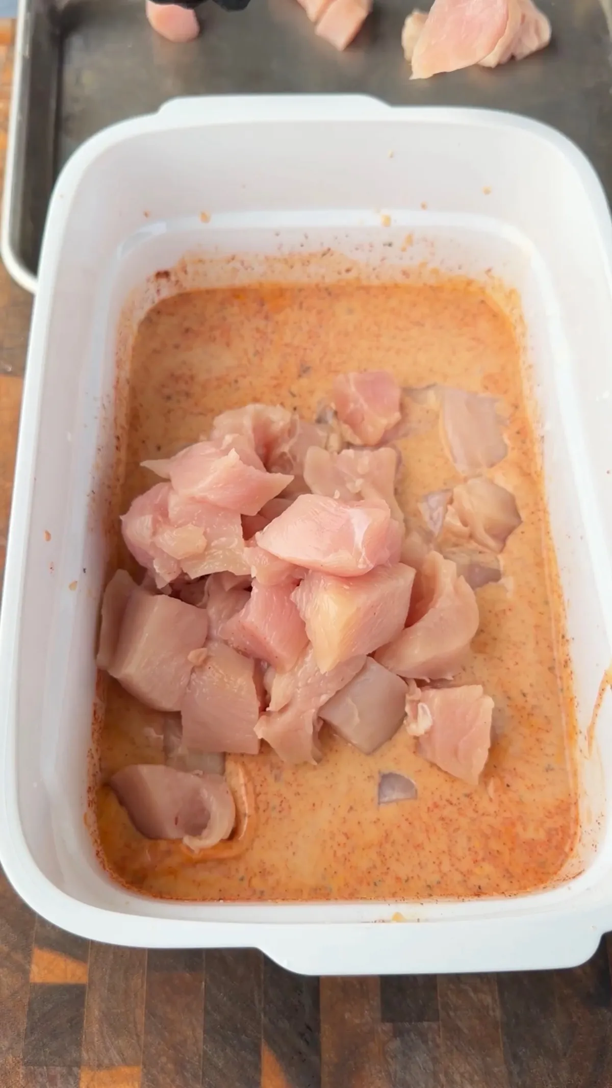 Raw chicken pieces marinating in seasoned buttermilk mixture in a white container for popcorn chicken