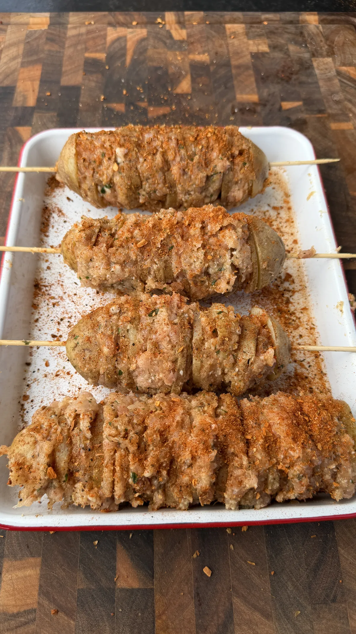 Raw garlic parmesan chicken and potato skewers on a white baking pan, seasoned with spices, ready to cook