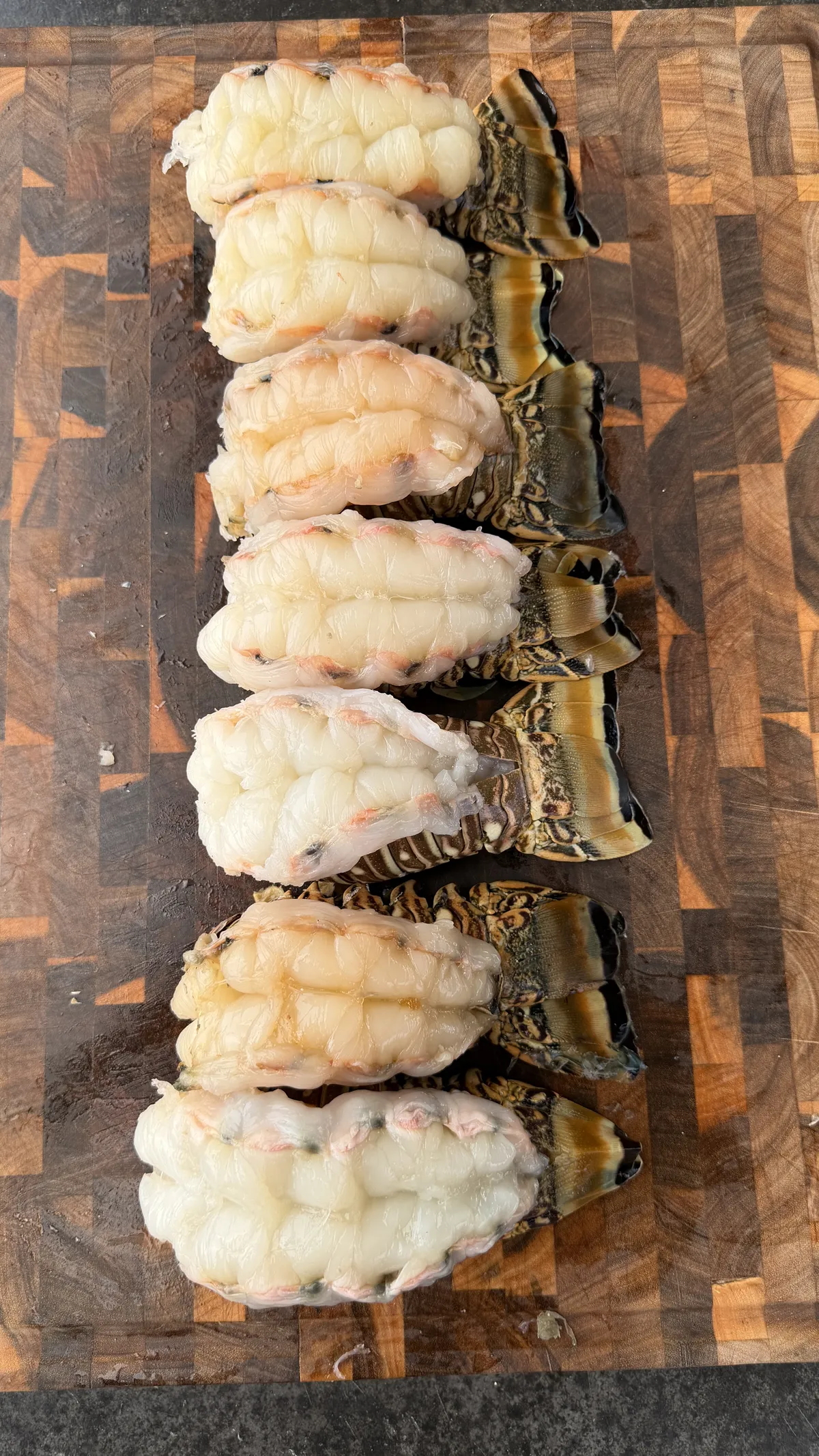 Six raw lobster tails with shell-on, lined up on a wooden end-grain cutting board, ready for smoking