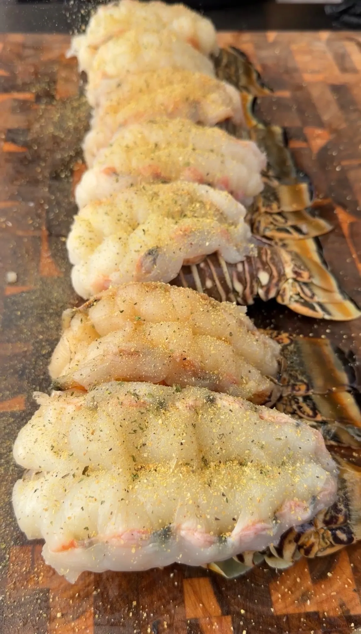 Raw lobster tails butterfly cut and seasoned with herbs and spices on a wooden cutting board