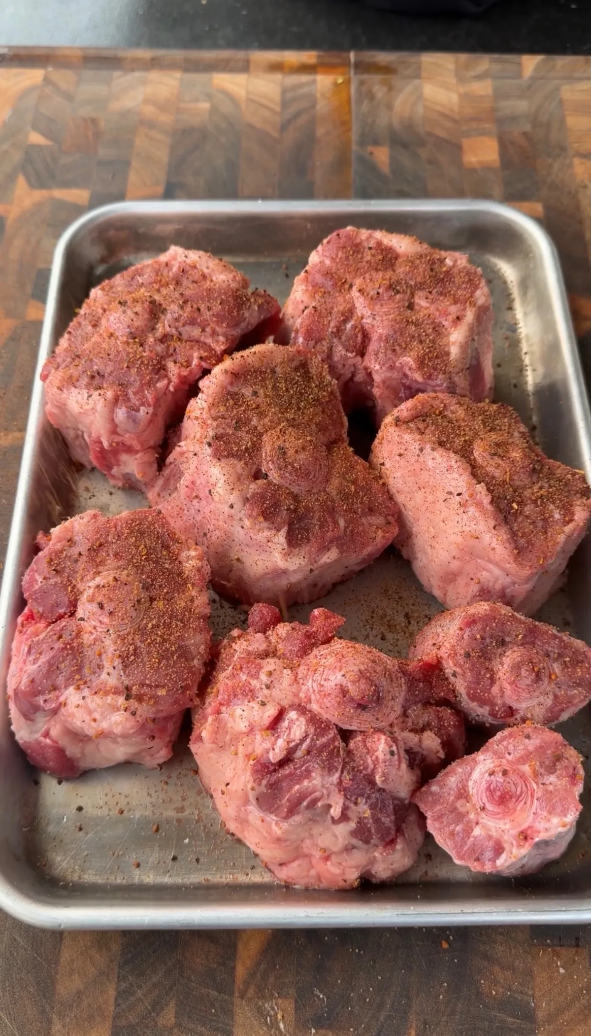 6 lbs beef oxtails generously seasoned with BBQ seasoning on a stainless steel tray, ready to smoke