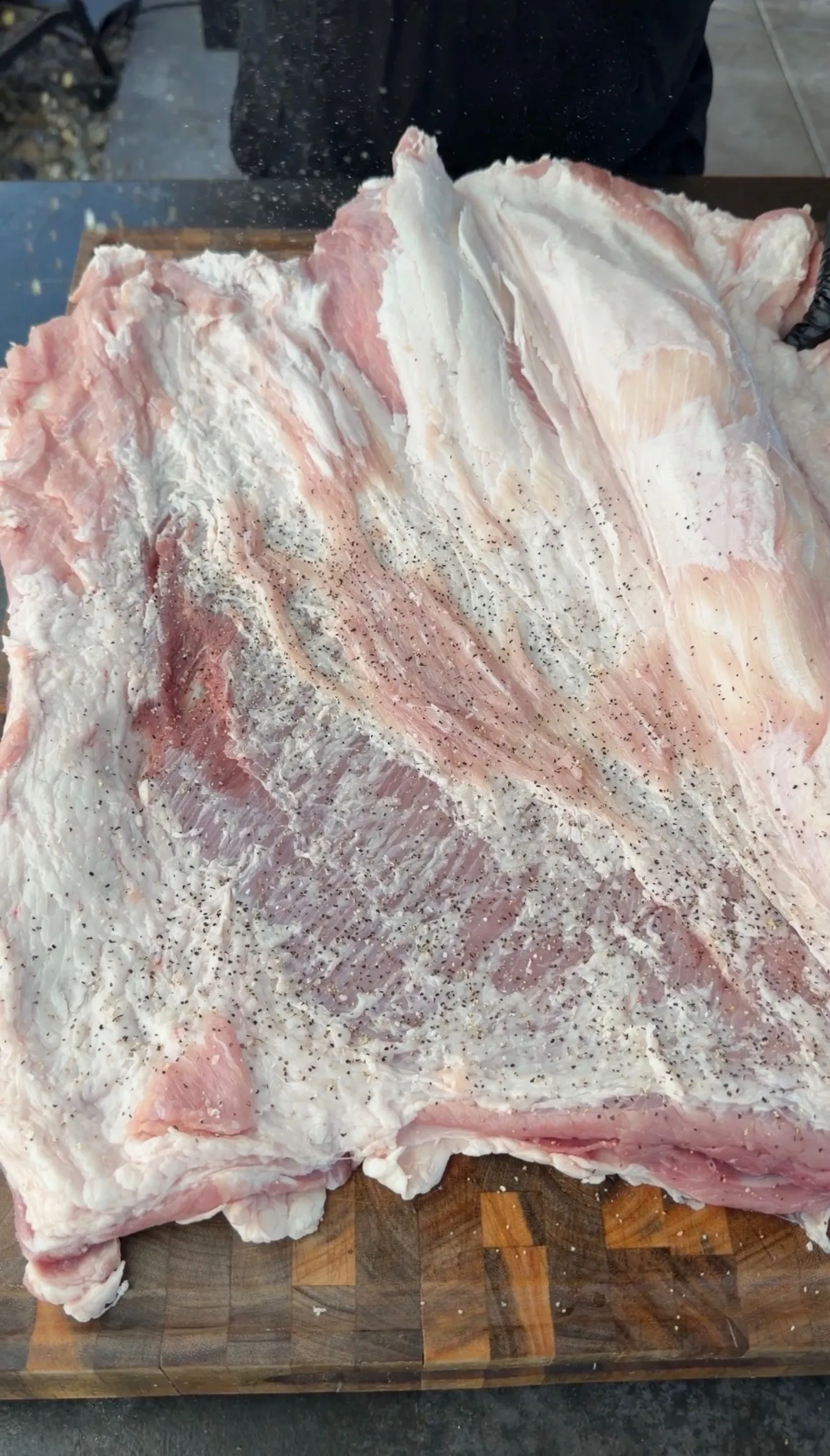 Raw pork belly skin-side up on a wooden cutting board, seasoned with salt and black pepper for Mexican adobo porchetta