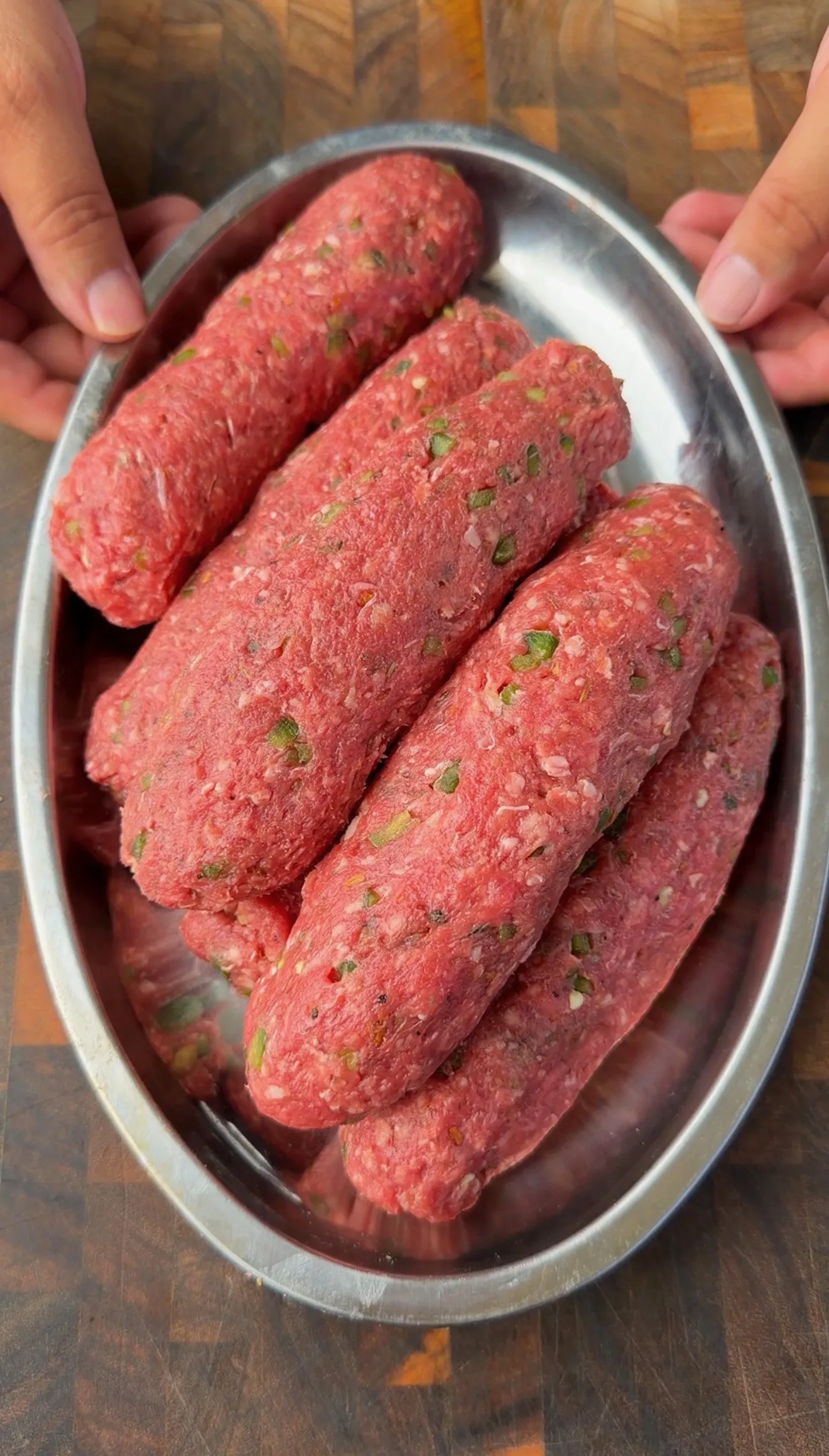 Raw seasoned ground beef logs shaped for cheese stuffed burger dogs on a silver oval tray