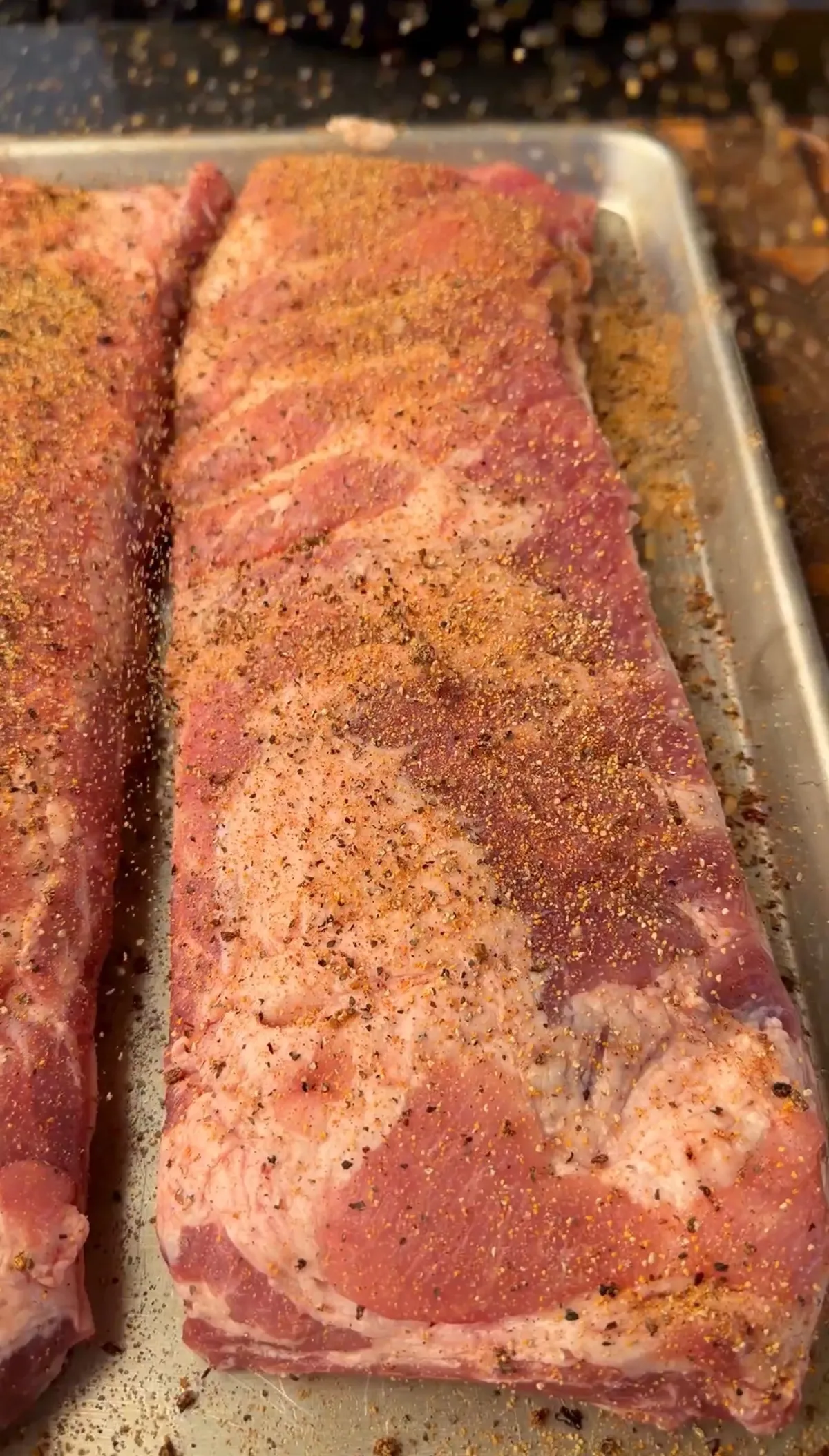 Raw St. Louis spare ribs seasoned with spiced dry rub on a metal baking sheet, ready for smoking