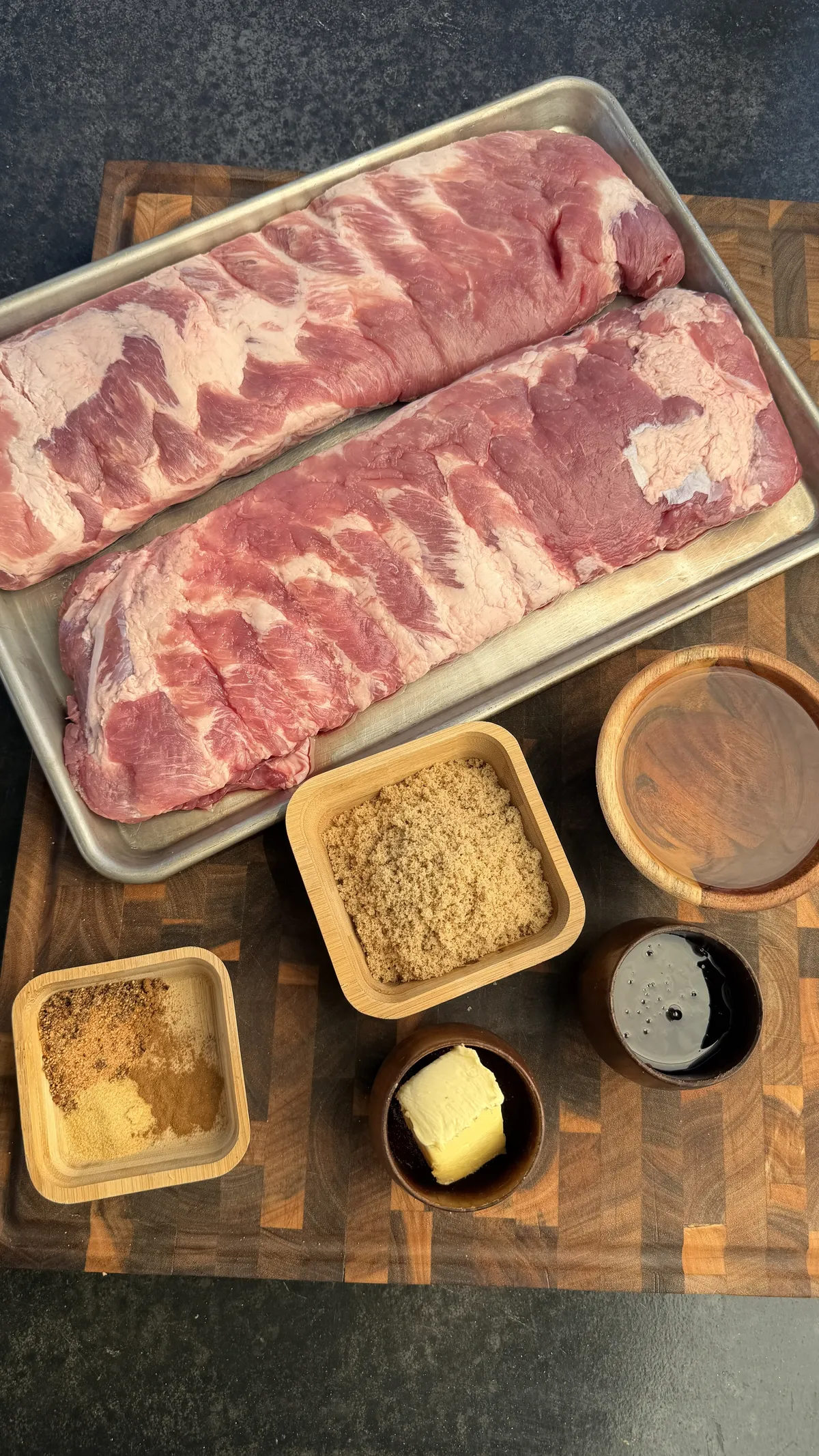 Raw St. Louis spare ribs in a pan with brown sugar, butter, spice rub, and apple cider glaze ingredients on a wood board