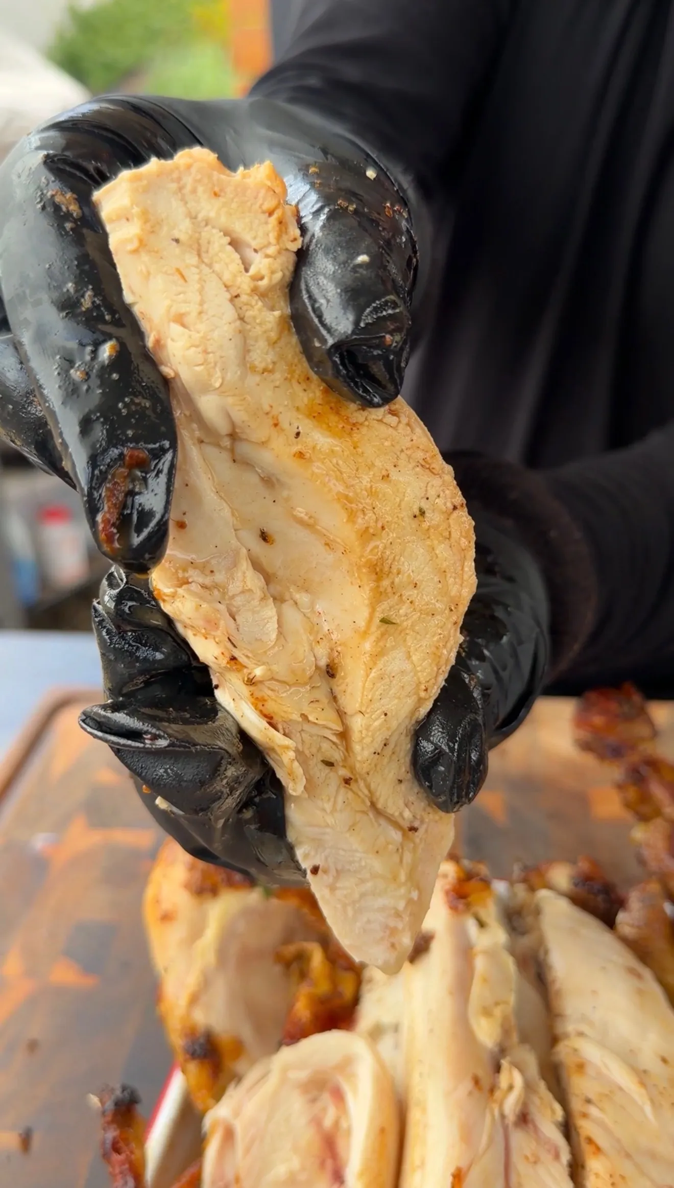 Gloved hands pulling apart juicy Cajun butter rotisserie chicken breast showing tender, seasoned white meat