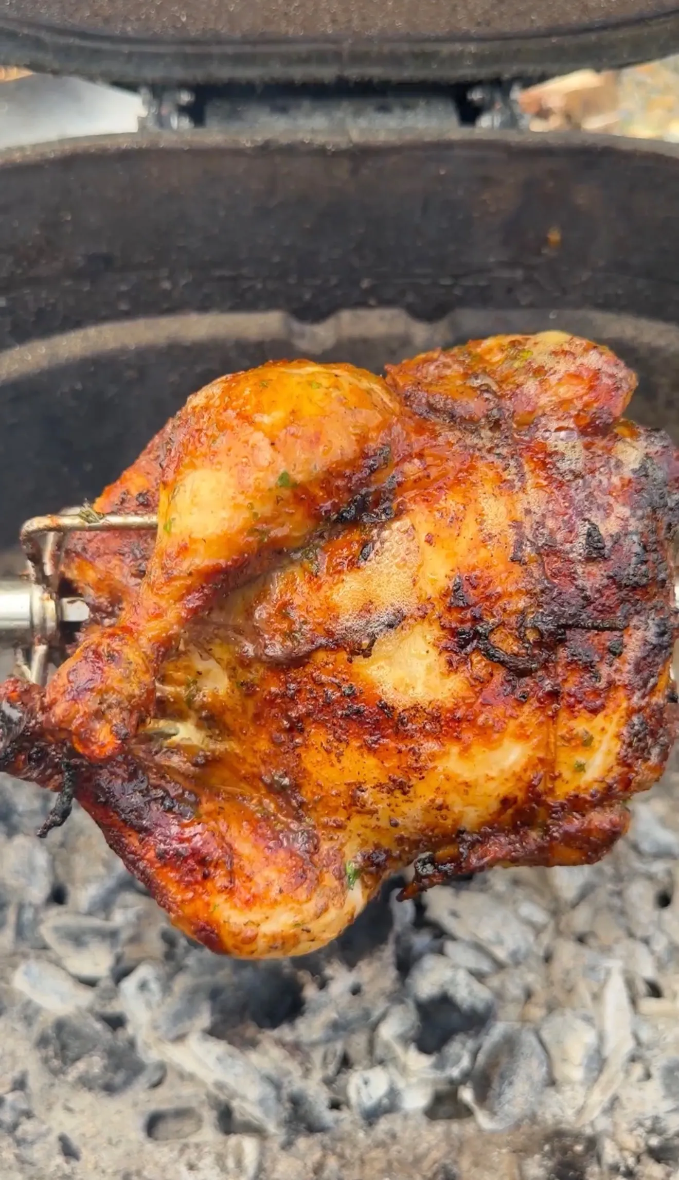 Whole rotisserie Cajun butter chicken on a spit over glowing charcoal with a crispy, spiced golden-brown crust