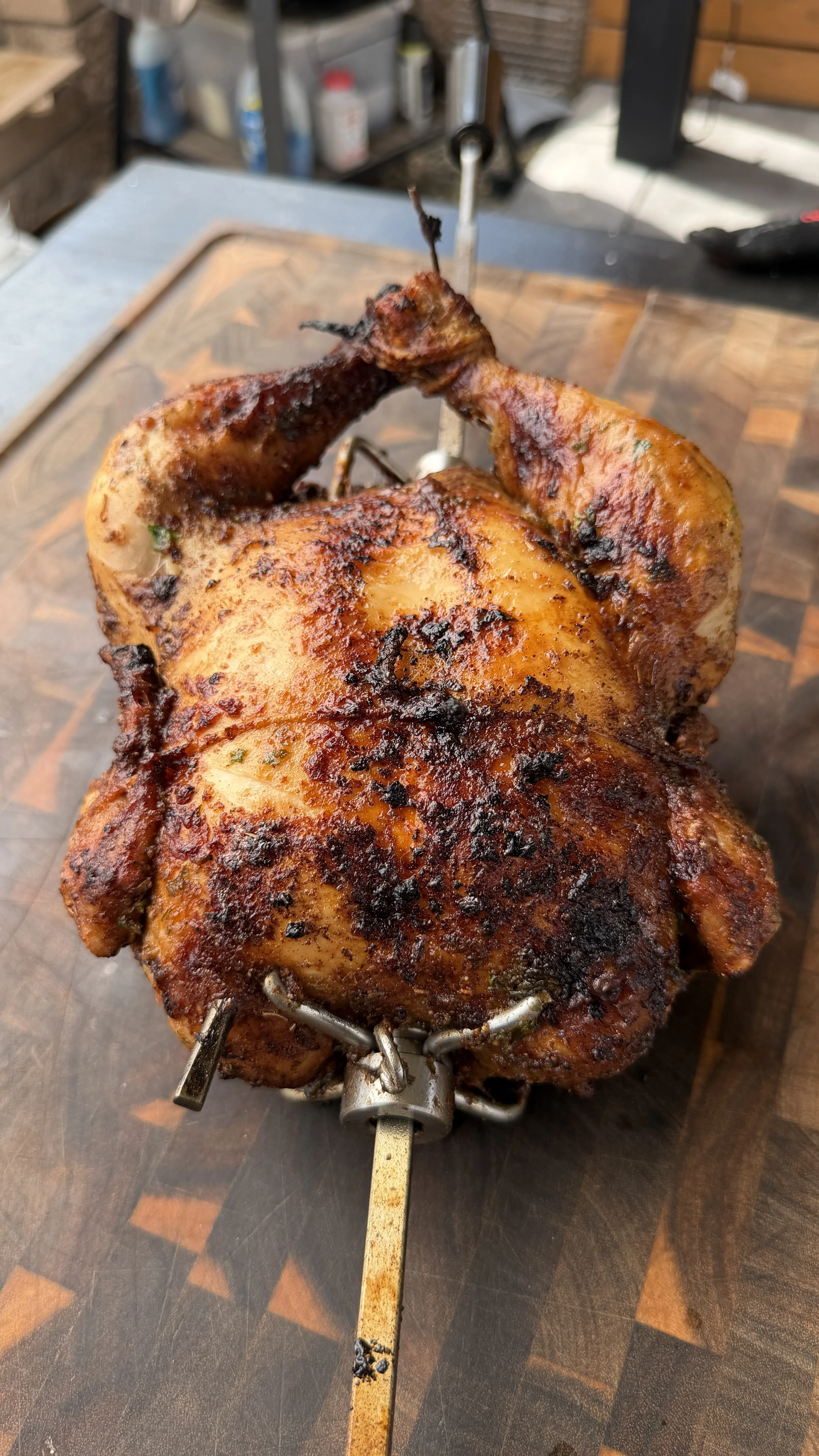 Whole Cajun butter rotisserie chicken on a spit with crispy, charred seasoned skin on a wooden cutting board