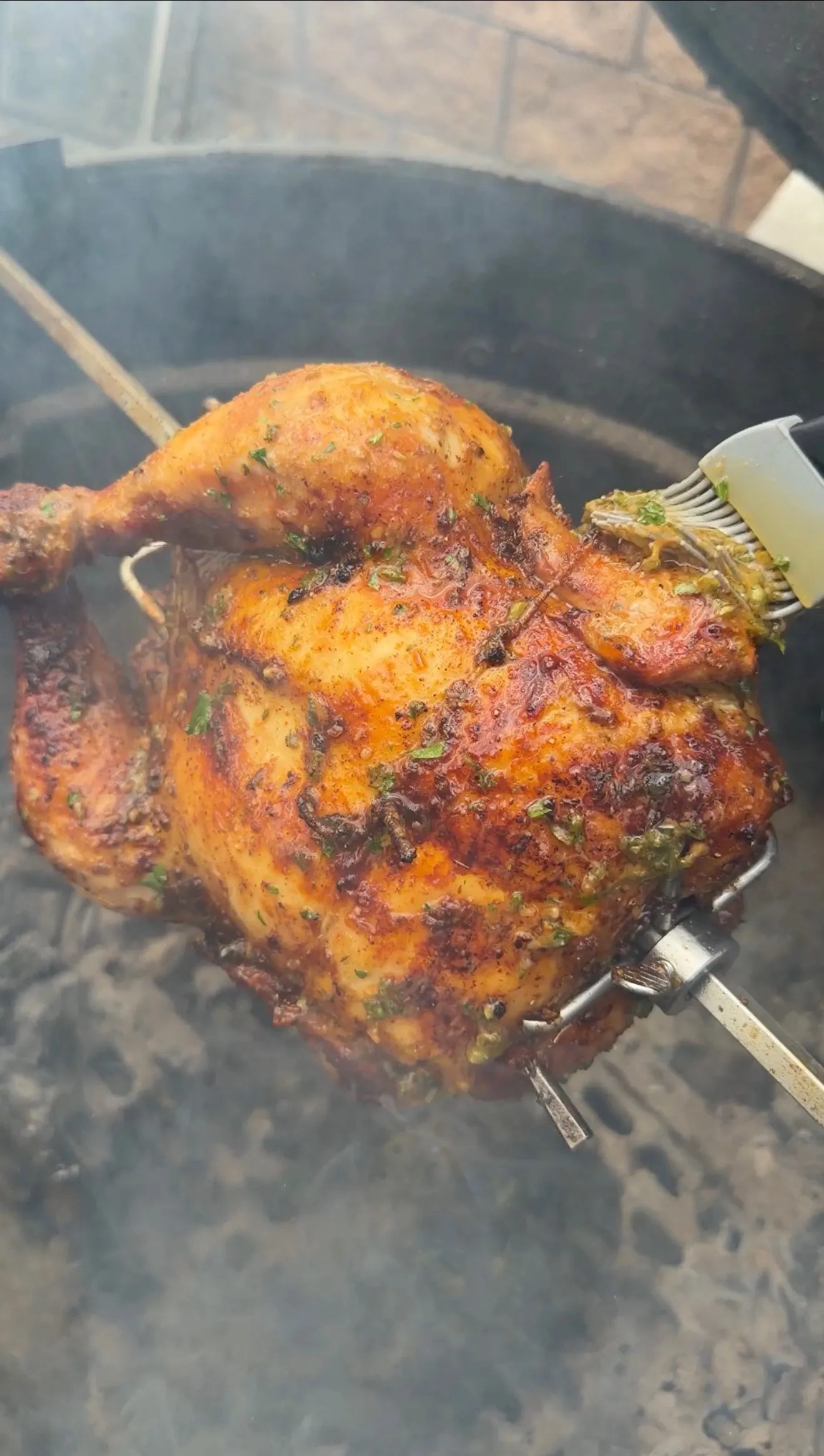 Whole rotisserie Cajun butter chicken on a spit being basted with herb butter on a smoky grill