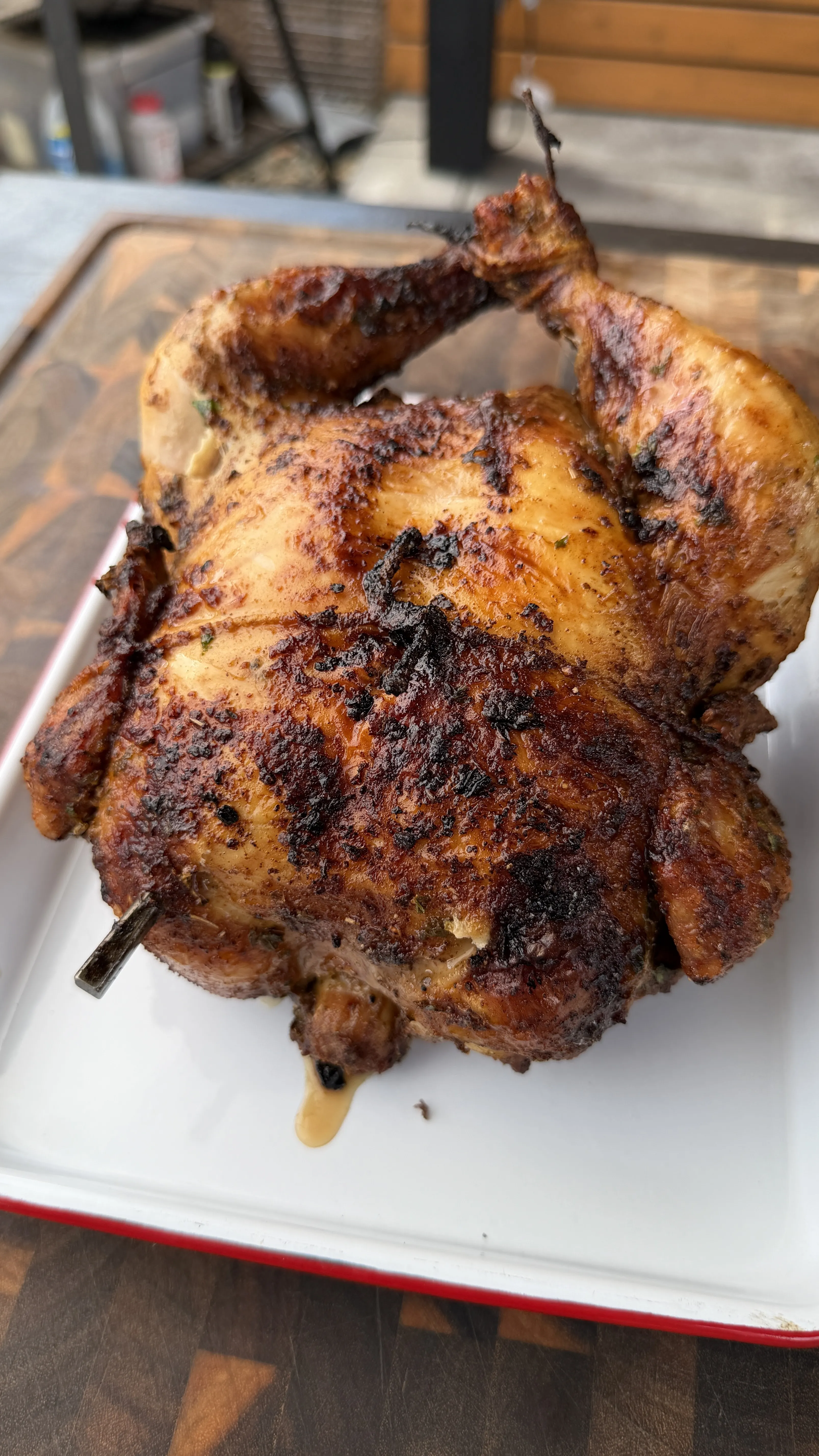 Whole rotisserie Cajun butter chicken with crispy, charred spiced skin on a white enamel tray
