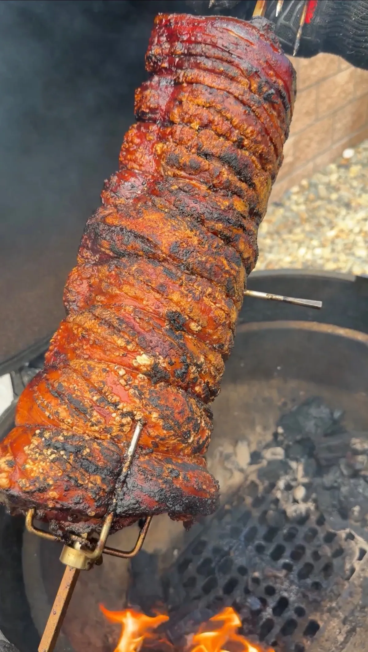 Crispy spice-rubbed pork belly porchetta rotating on a rotisserie spit over hot charcoal flames