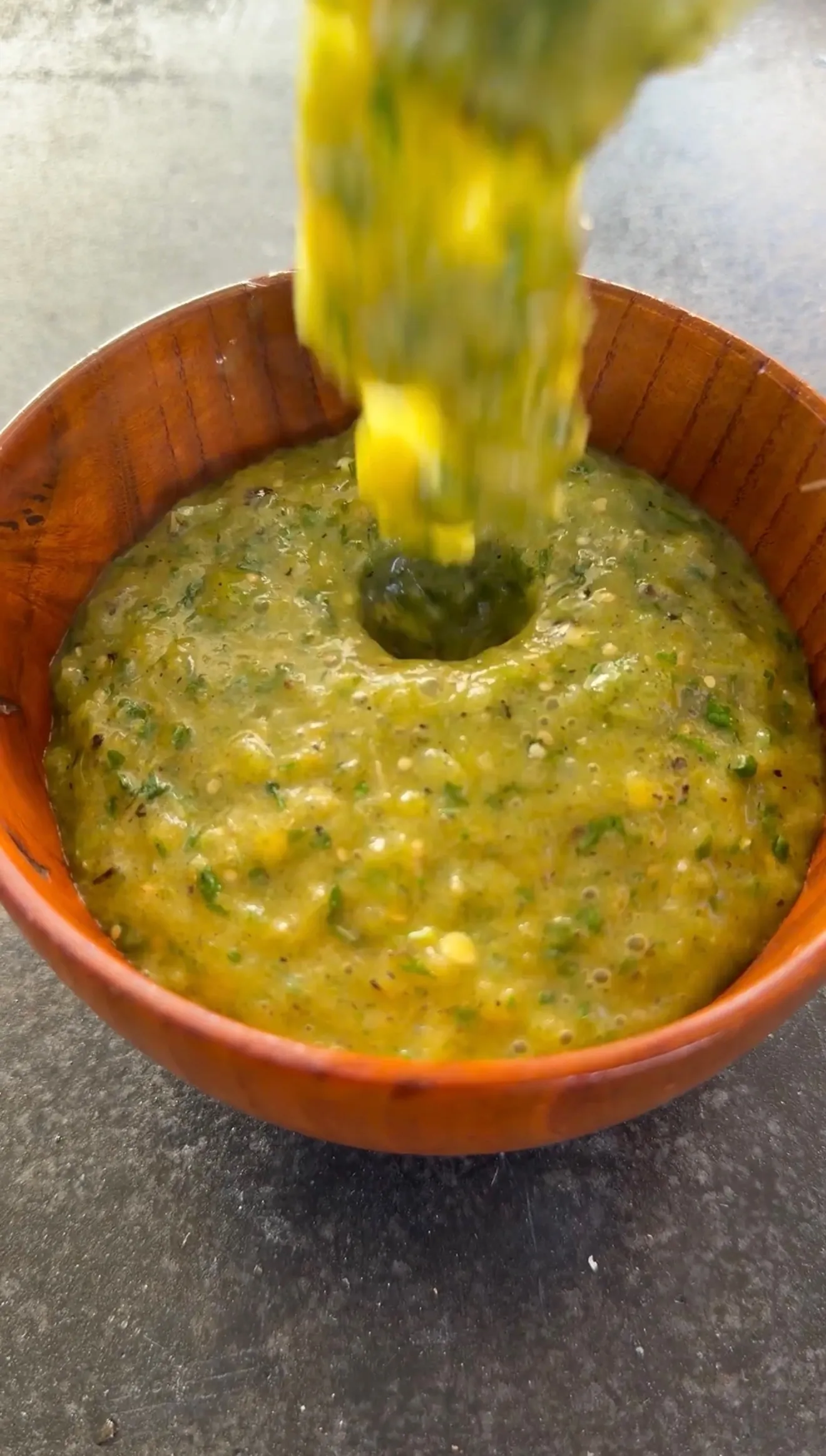 Chunky salsa verde being poured into a rustic wooden bowl, made with tomatillos, cilantro, and peppers