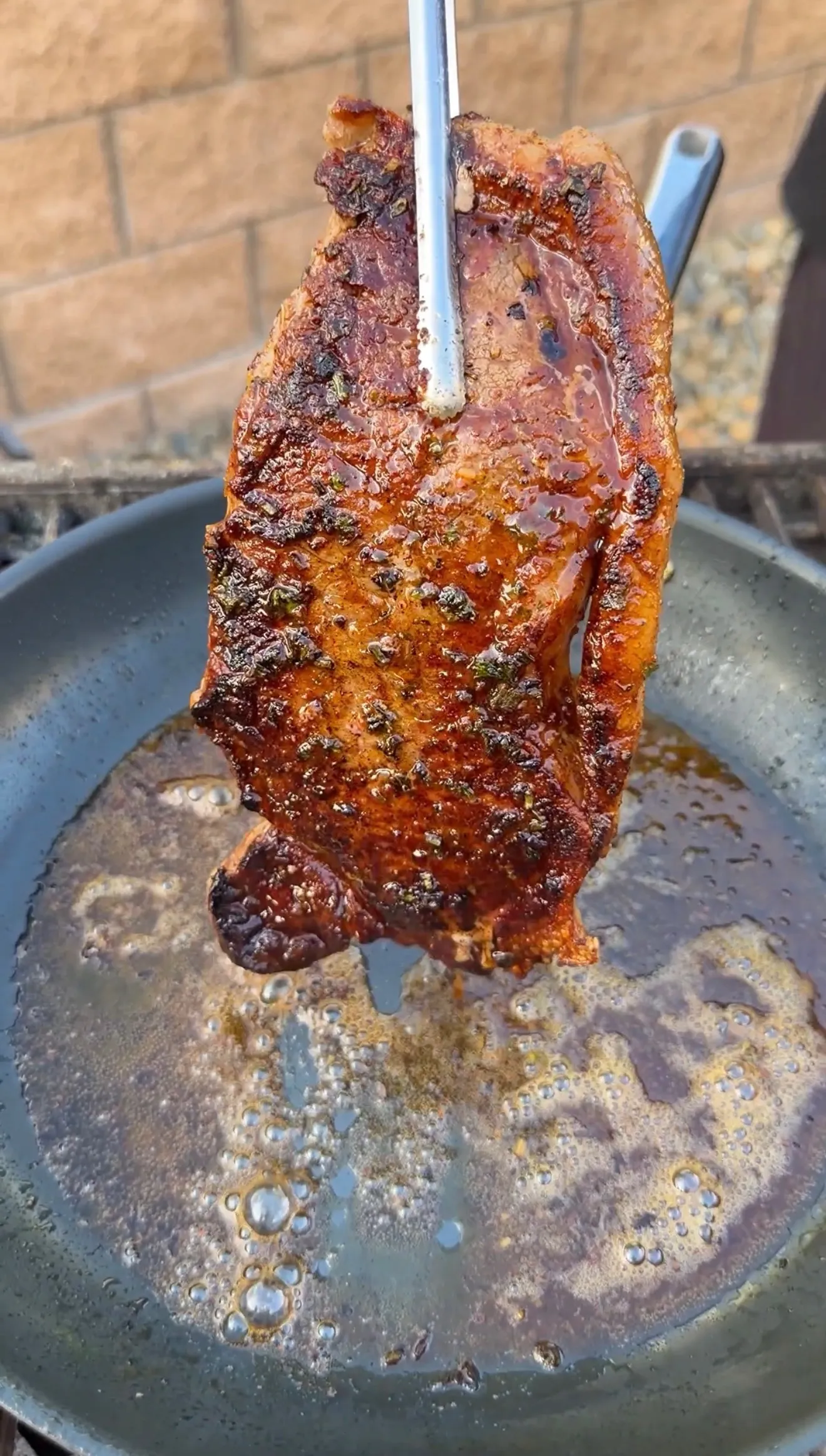 Seasoned seared steak held by tongs over a sizzling cast iron skillet with melted cowboy butter