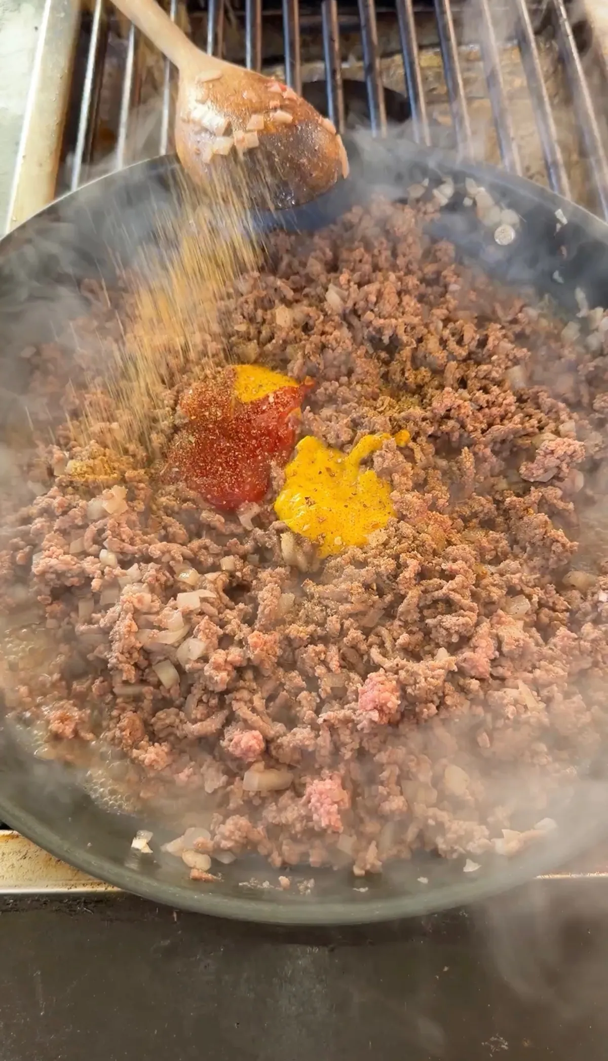 Ground beef browning in a hot skillet with tomato paste, turmeric, and spices being added for cheeseburger filling