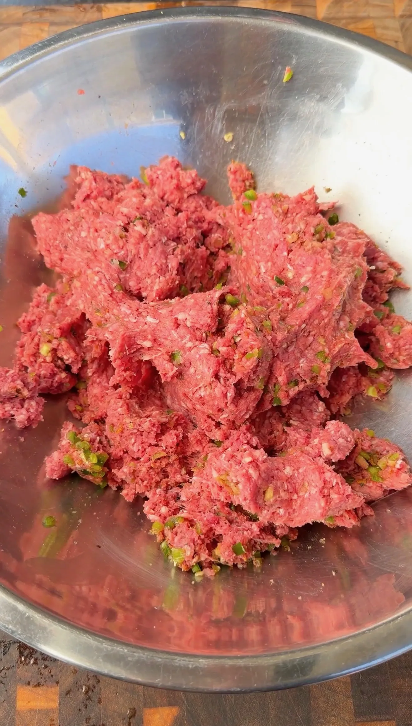 Raw seasoned ground beef mixed with diced jalapeños in a stainless steel mixing bowl for burger dogs