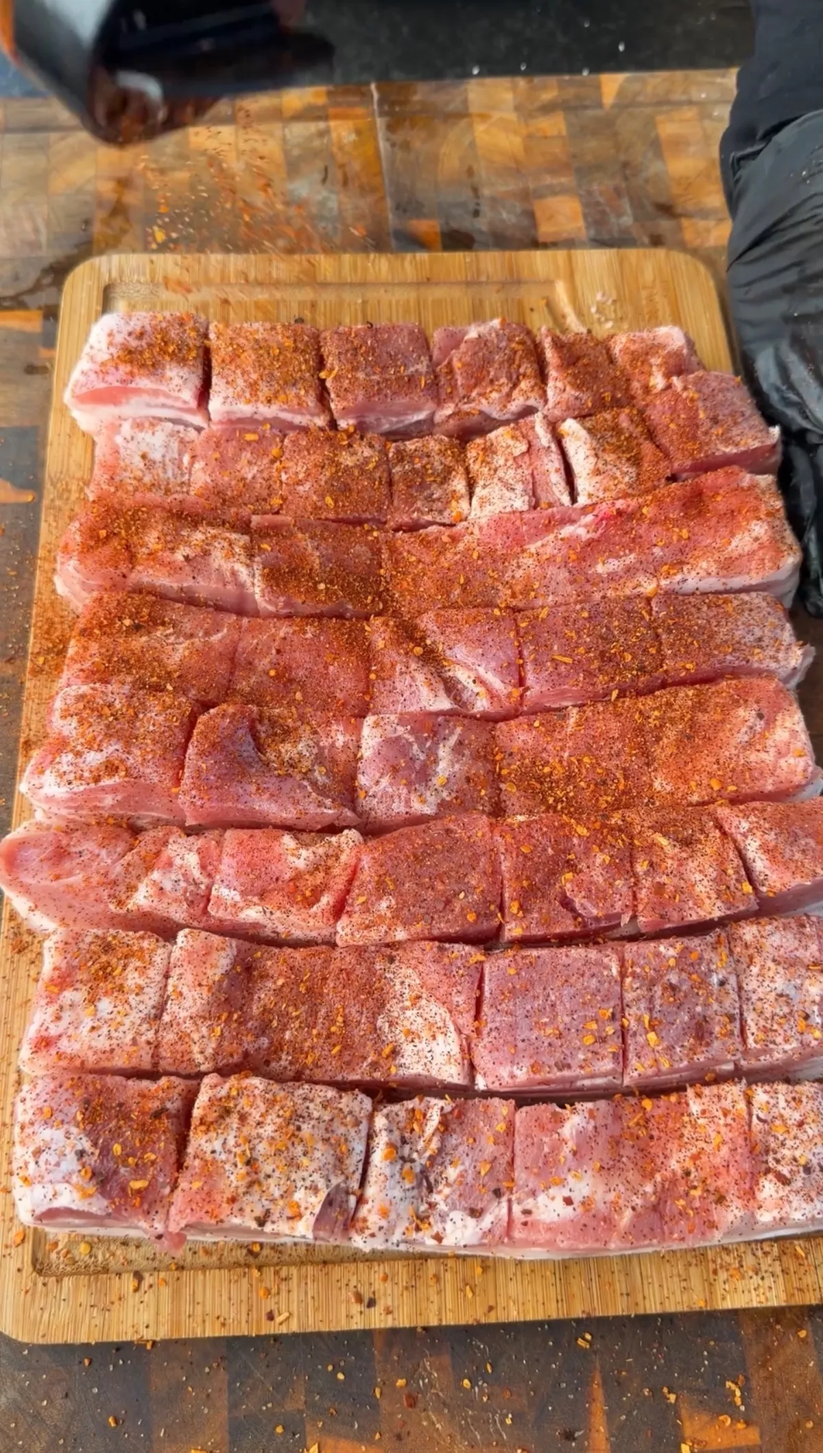 Raw scored pork belly slabs coated in red chili spice rub on a wooden cutting board for chicharron tacos