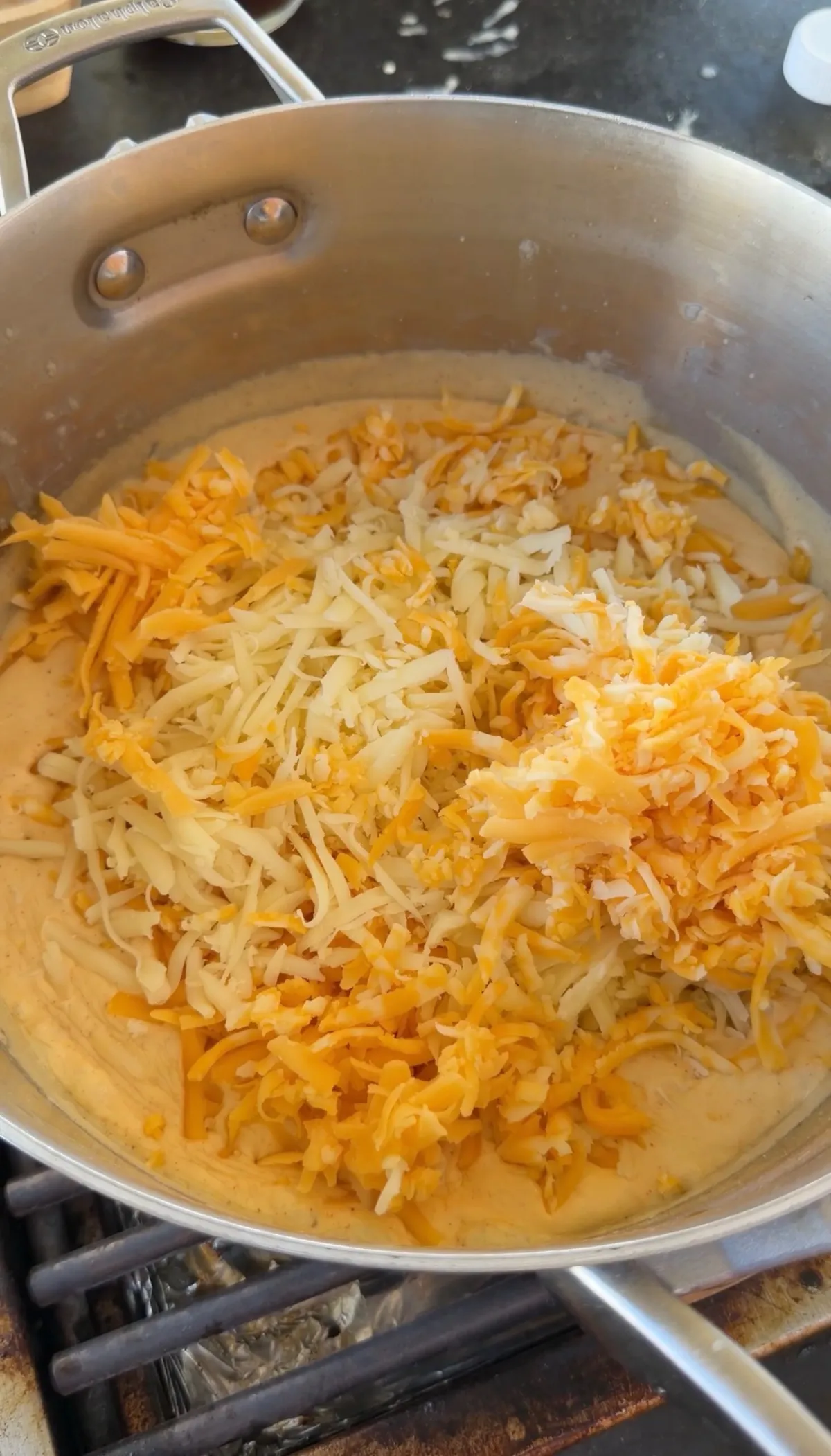 Freshly shredded mozzarella, Colby Jack, and sharp cheddar added to creamy cheese sauce in stainless skillet